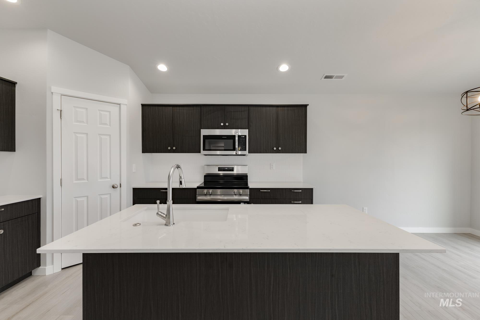 Kitchen featuring stainless steel appliances, a center island with sink, light stone counters, light wood finished floors, and recessed lighting