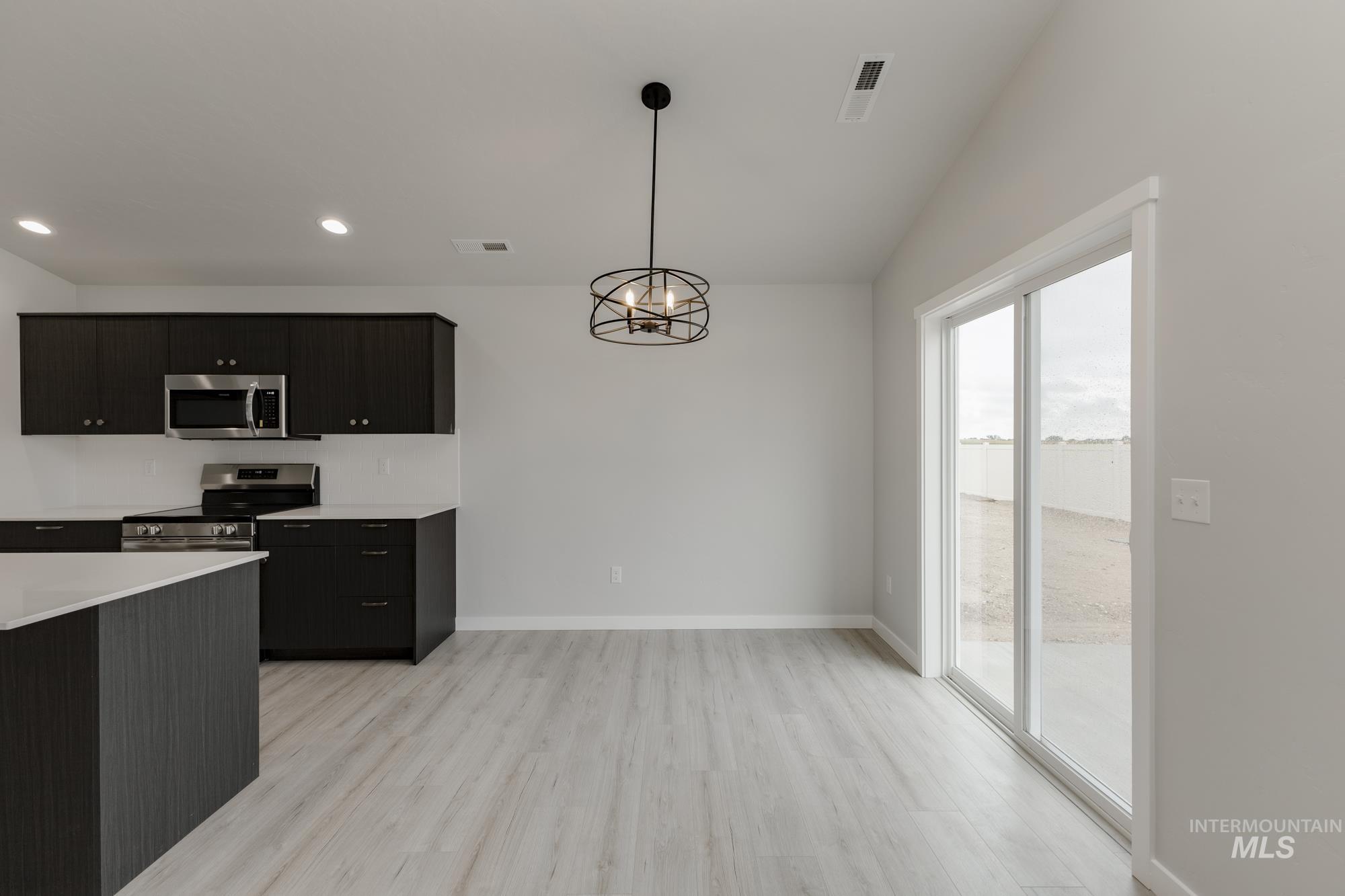 Kitchen featuring light wood finished floors, pendant lighting, appliances with stainless steel finishes, dark cabinets, and a chandelier