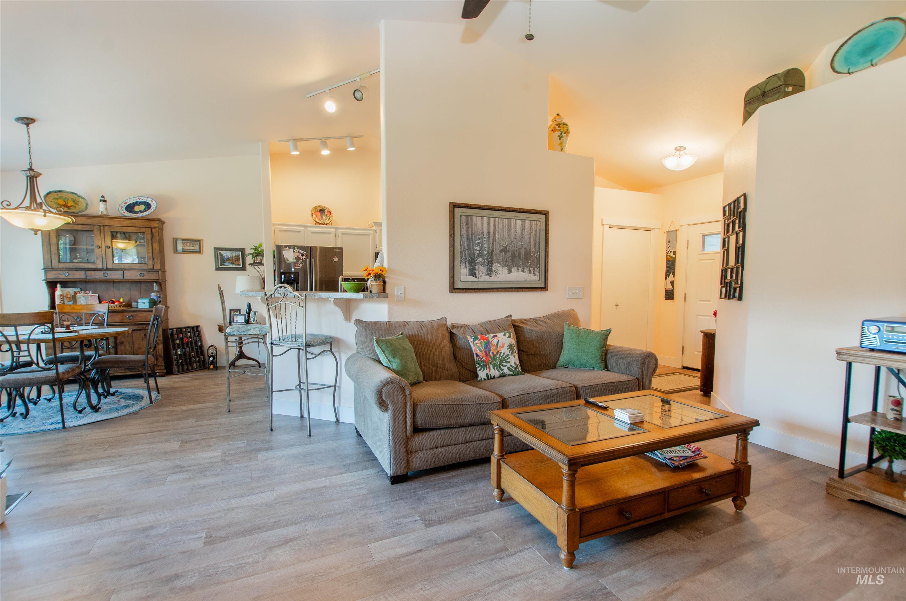 Living room featuring light wood-style floors, ceiling fan, lofted ceiling, and rail lighting
