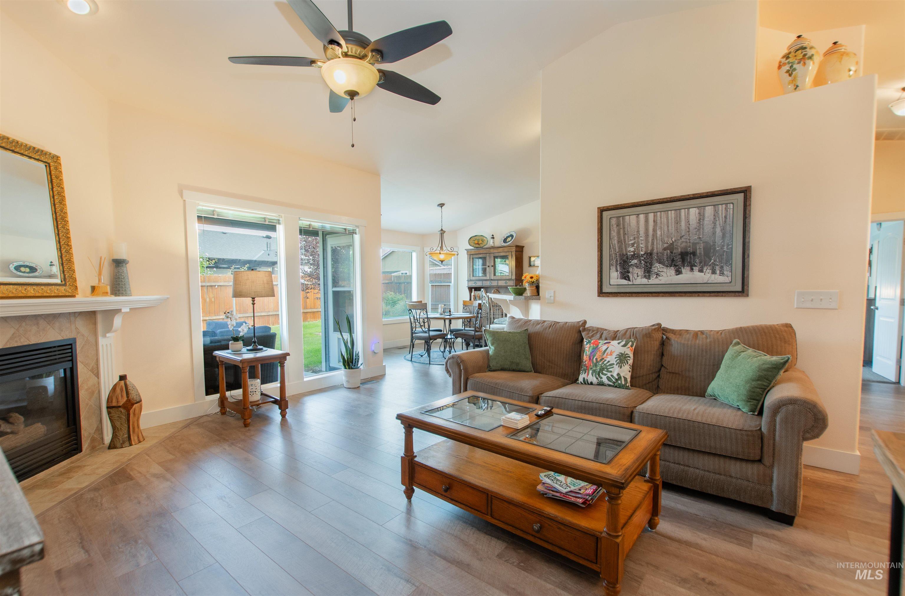 Living room featuring wood finished floors, a tiled fireplace, ceiling fan, and high vaulted ceiling
