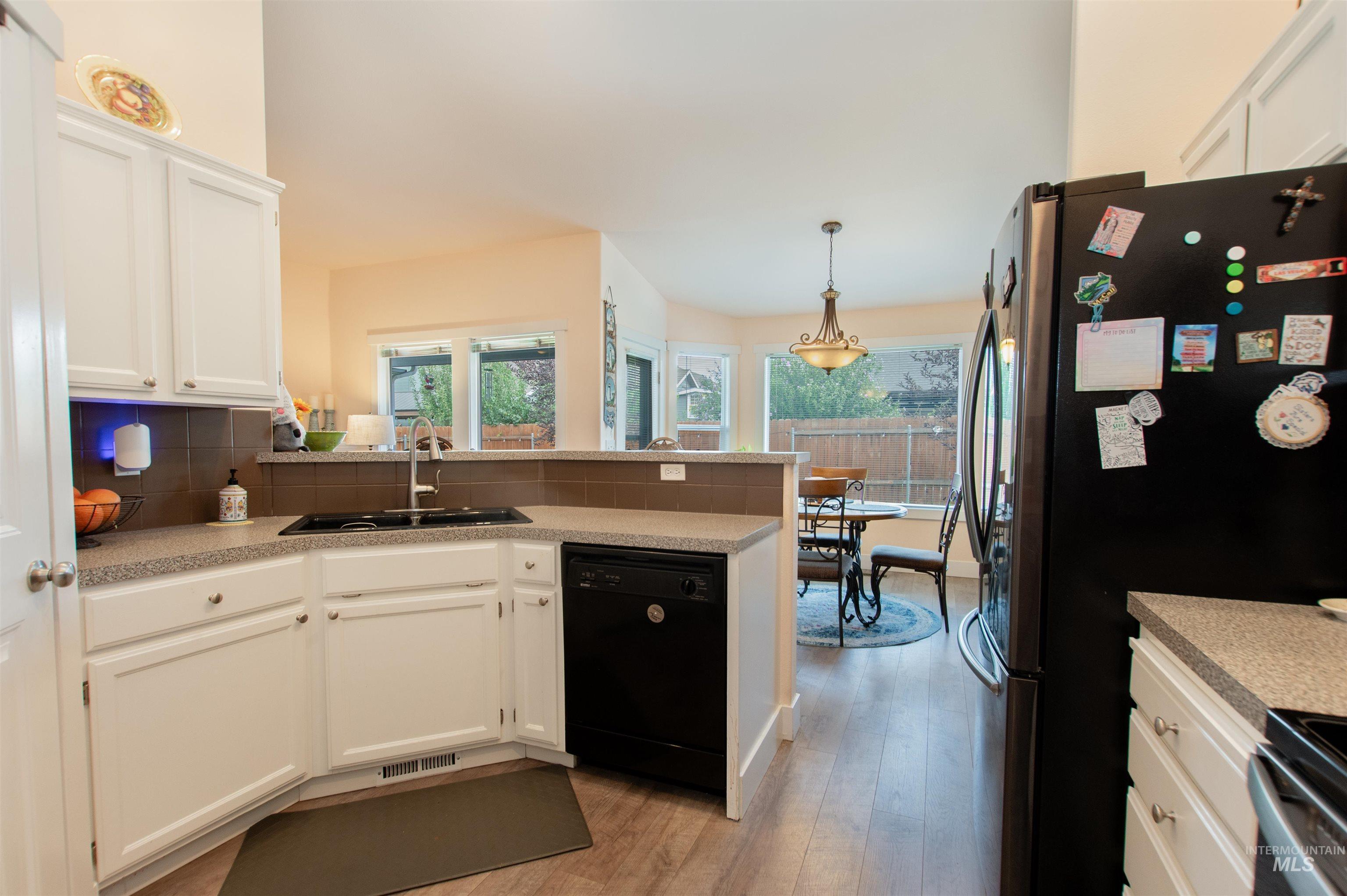 Kitchen with white cabinets, backsplash, light wood finished floors, appliances with stainless steel finishes, and a peninsula