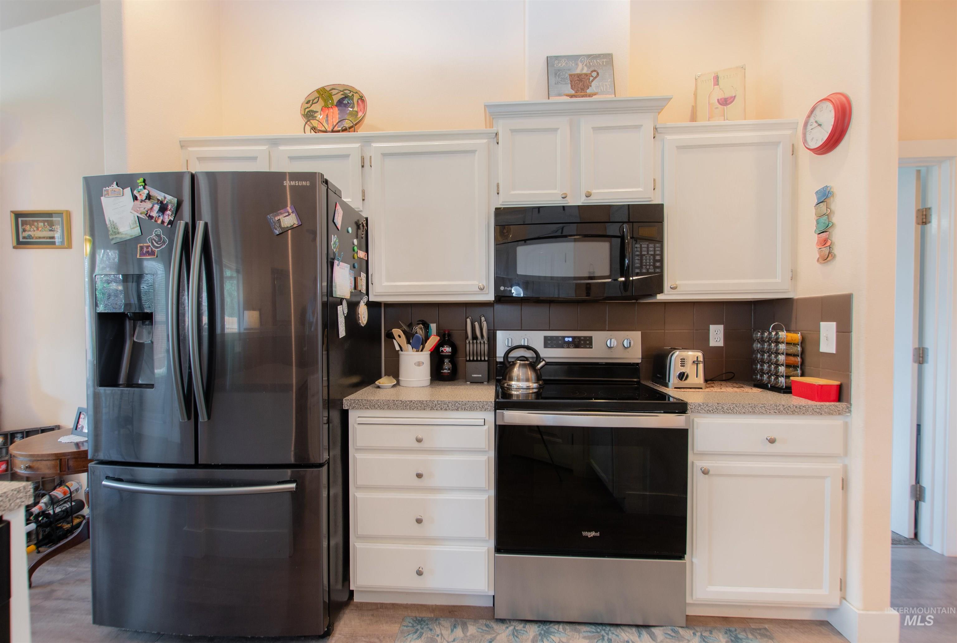 Kitchen with appliances with stainless steel finishes, tasteful backsplash, light countertops, and white cabinets