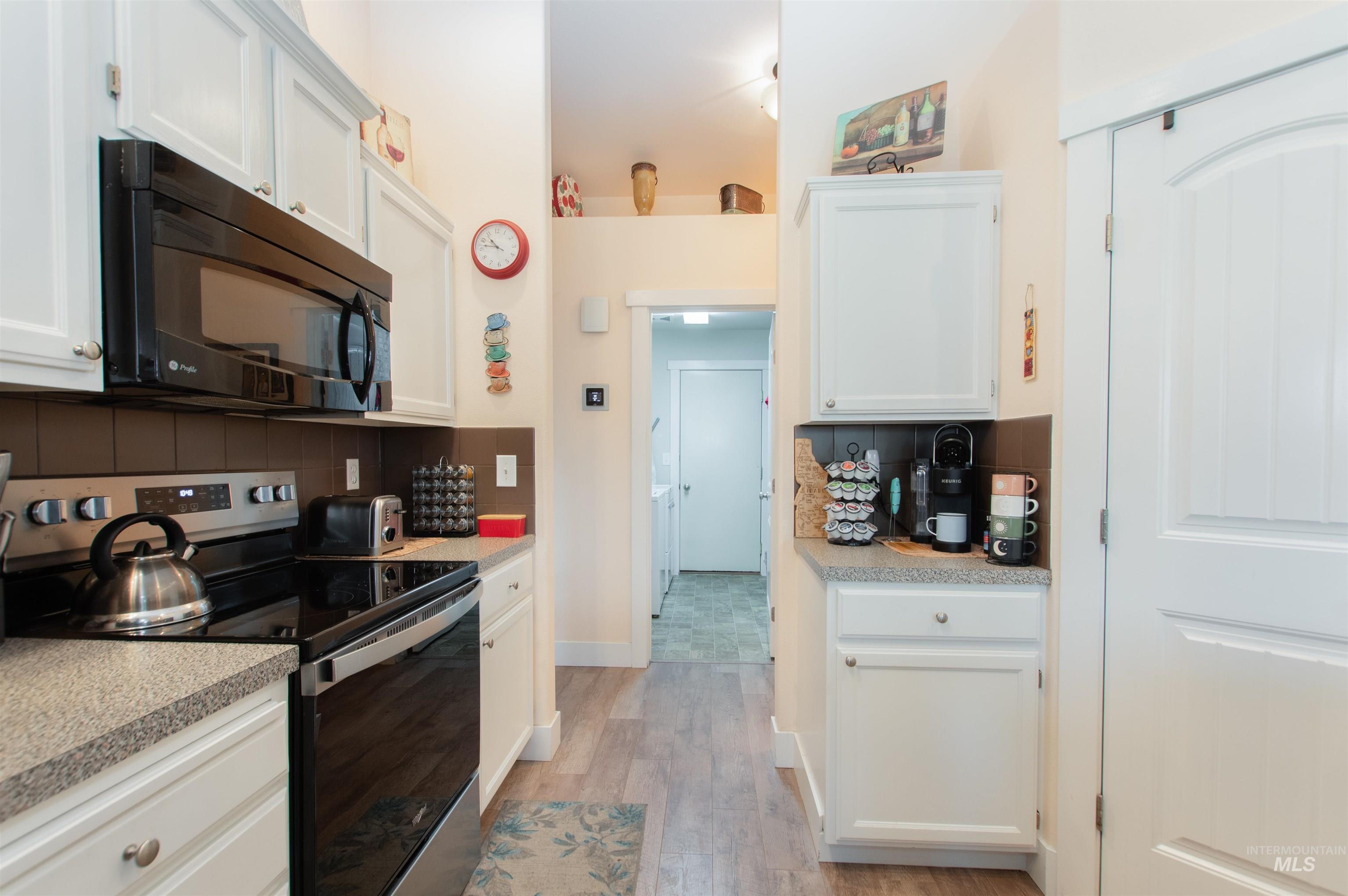 Kitchen with stainless steel range with electric stovetop, black microwave, white cabinets, and light wood-style flooring