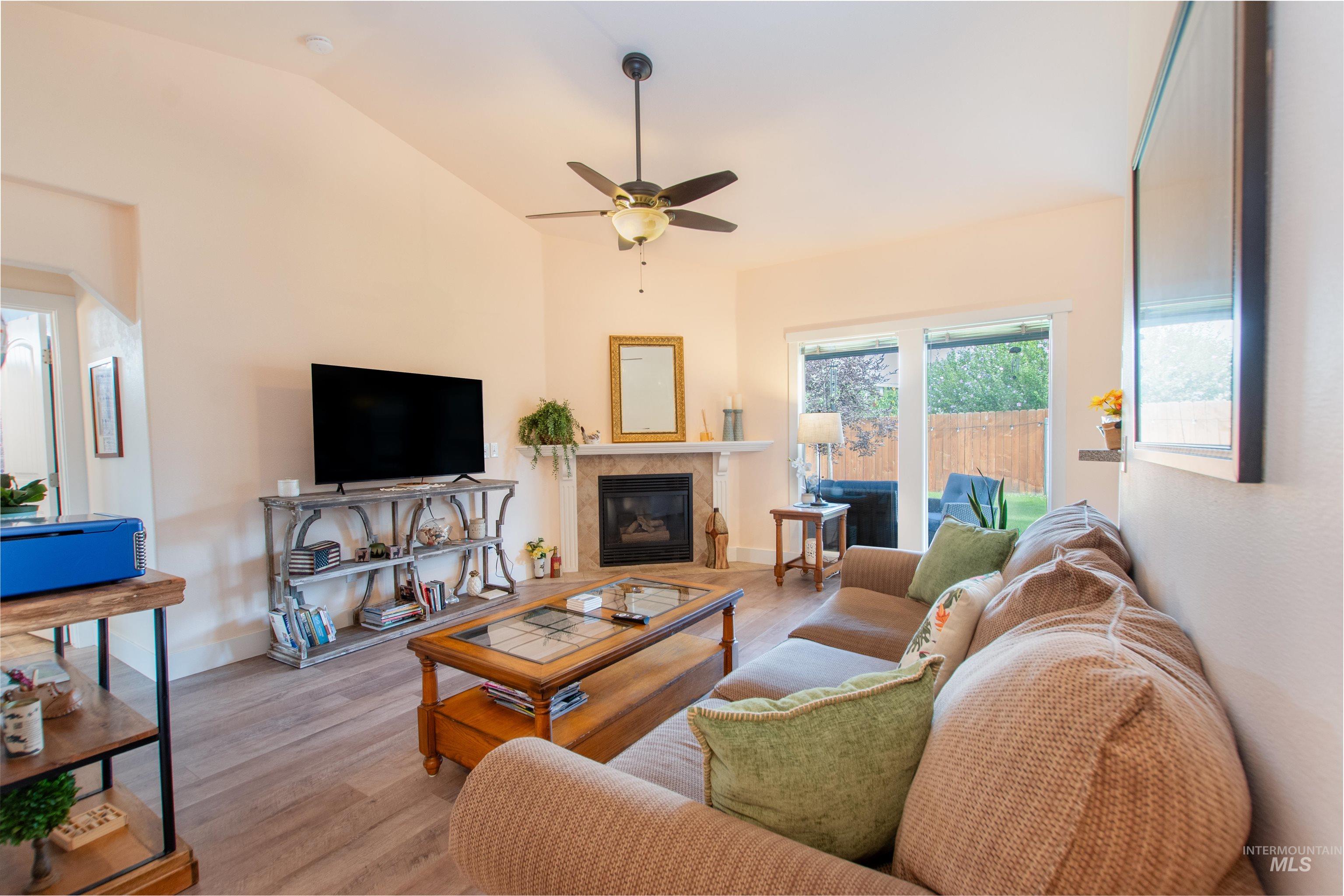 Living room with a fireplace, wood finished floors, a ceiling fan, and vaulted ceiling