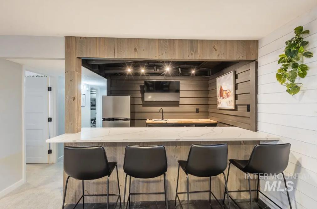 Kitchen with freestanding refrigerator, wood walls, a peninsula, a kitchen bar, and light stone counters