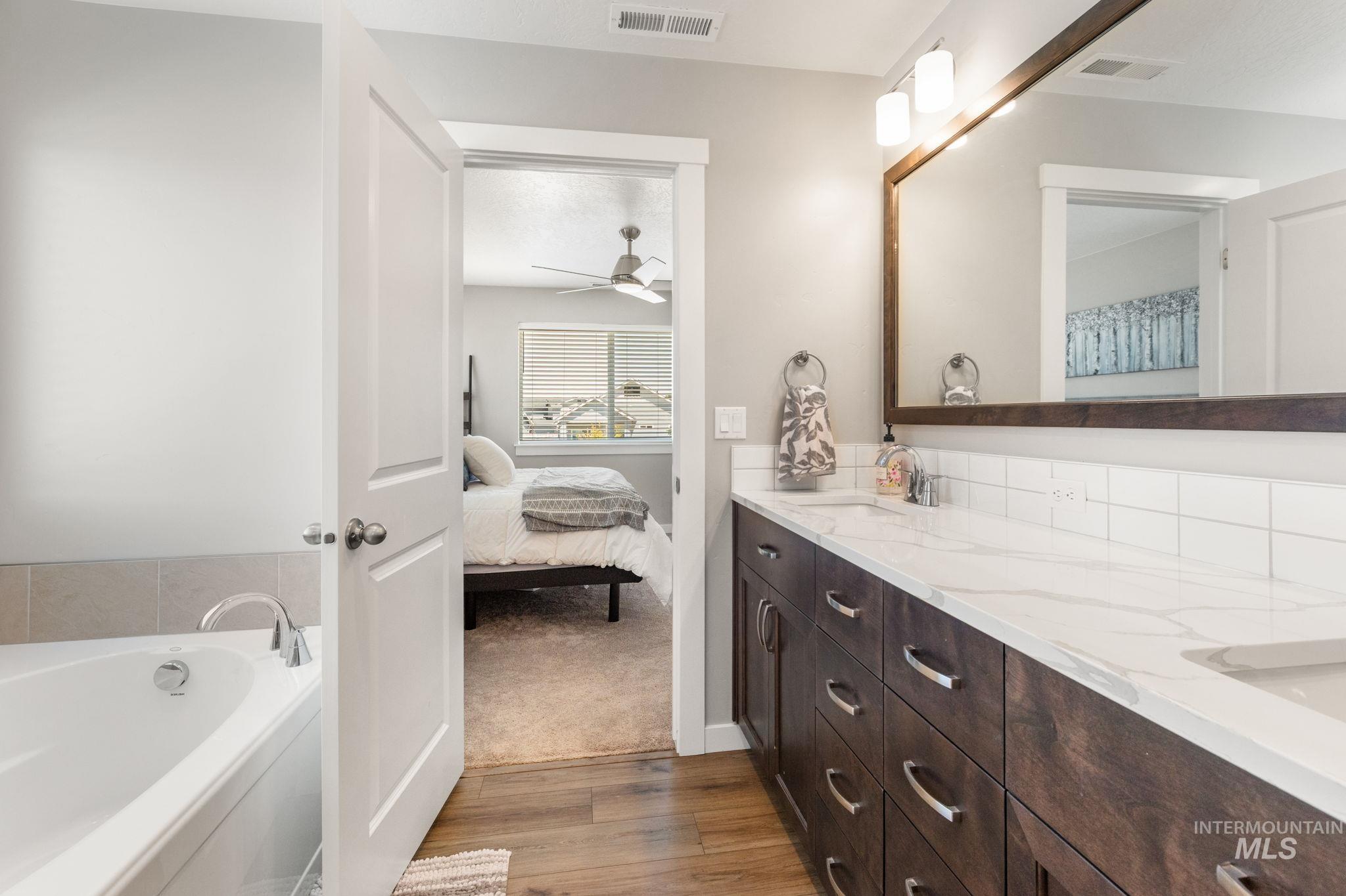 Full bath featuring wood finished floors, double vanity, ensuite bath, a bath, and a ceiling fan