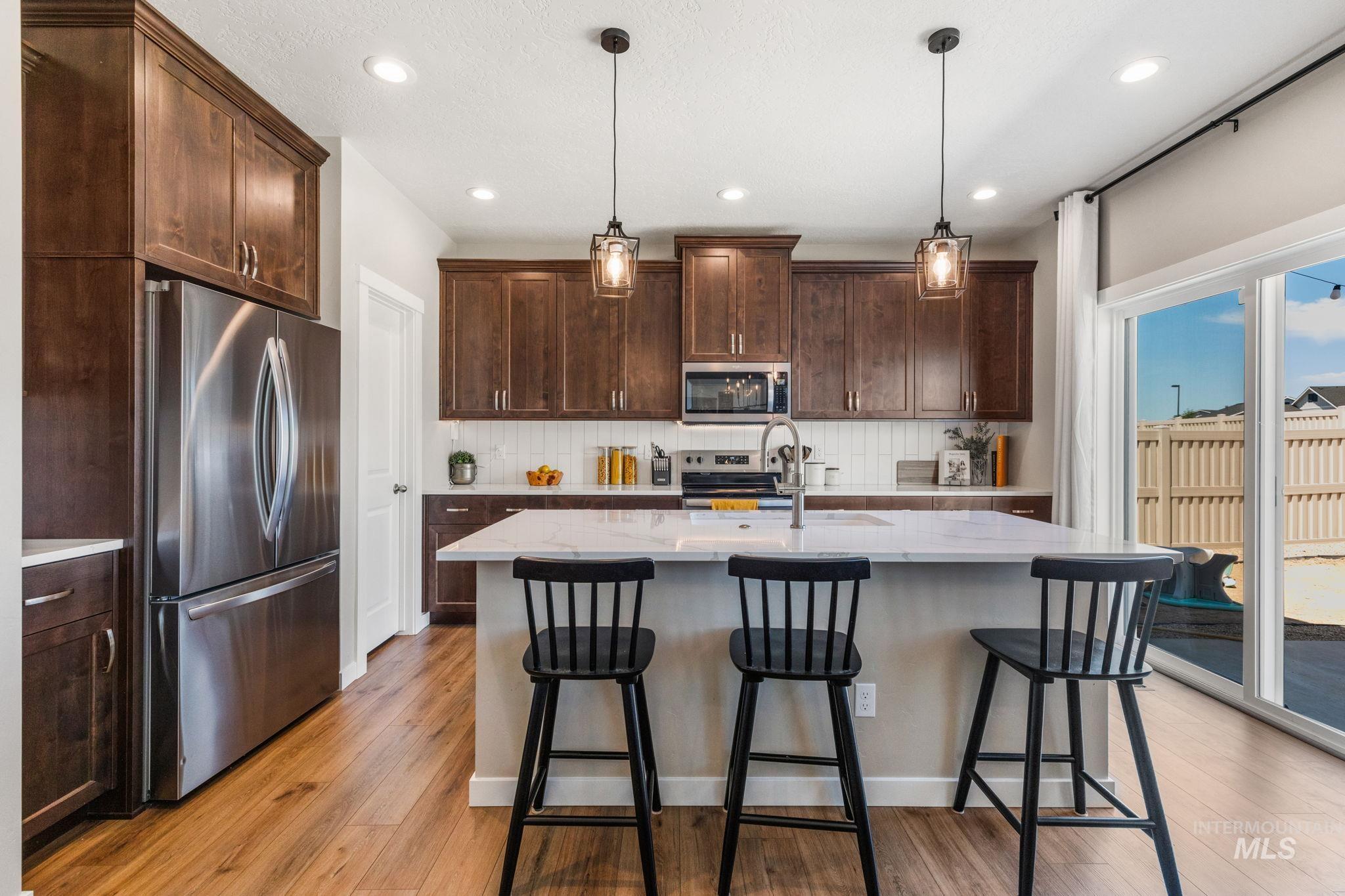 Kitchen featuring appliances with stainless steel finishes, dark brown cabinets, tasteful backsplash, light wood-type flooring, and a kitchen bar