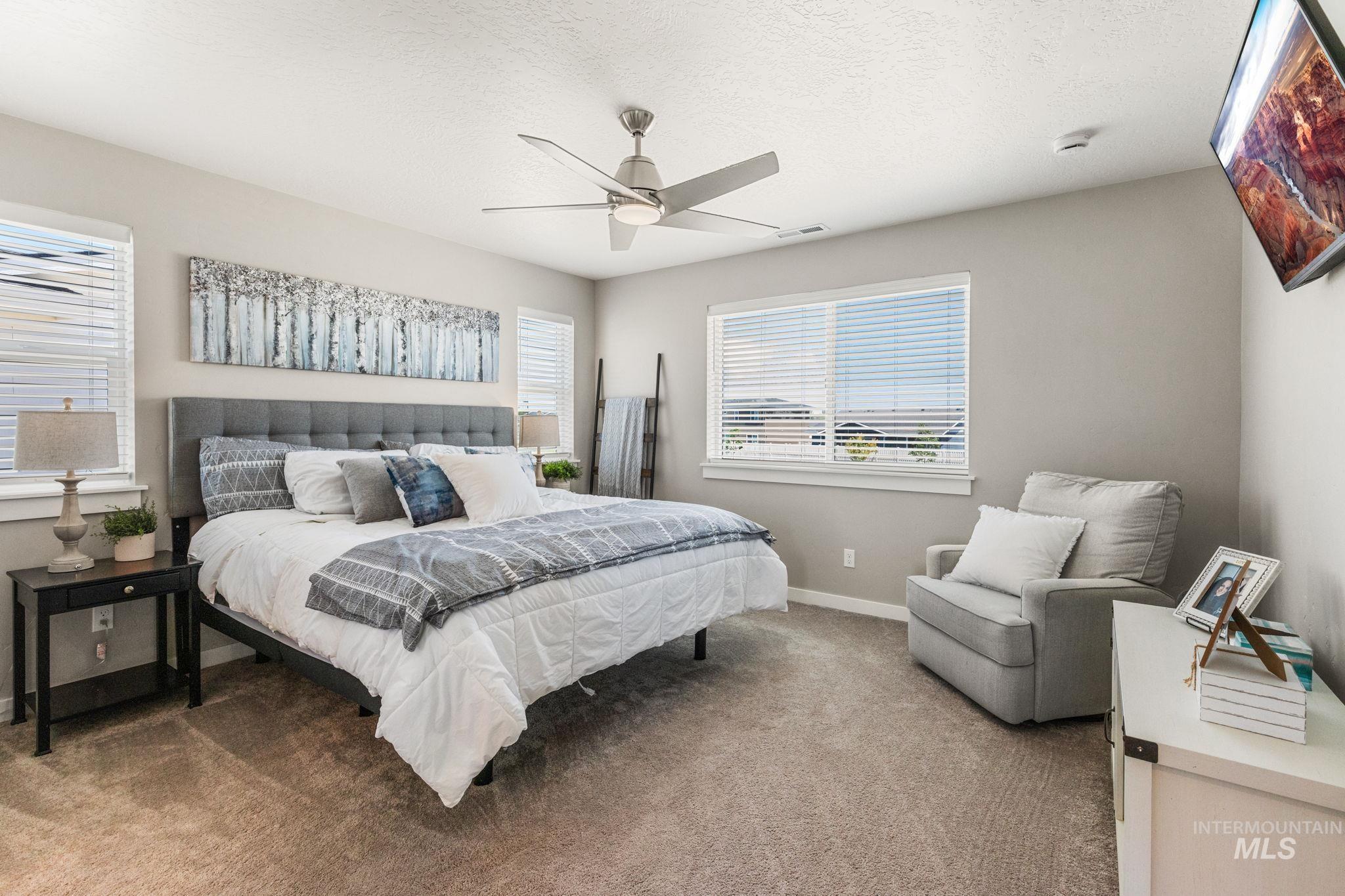 Carpeted bedroom featuring multiple windows, a textured ceiling, and ceiling fan