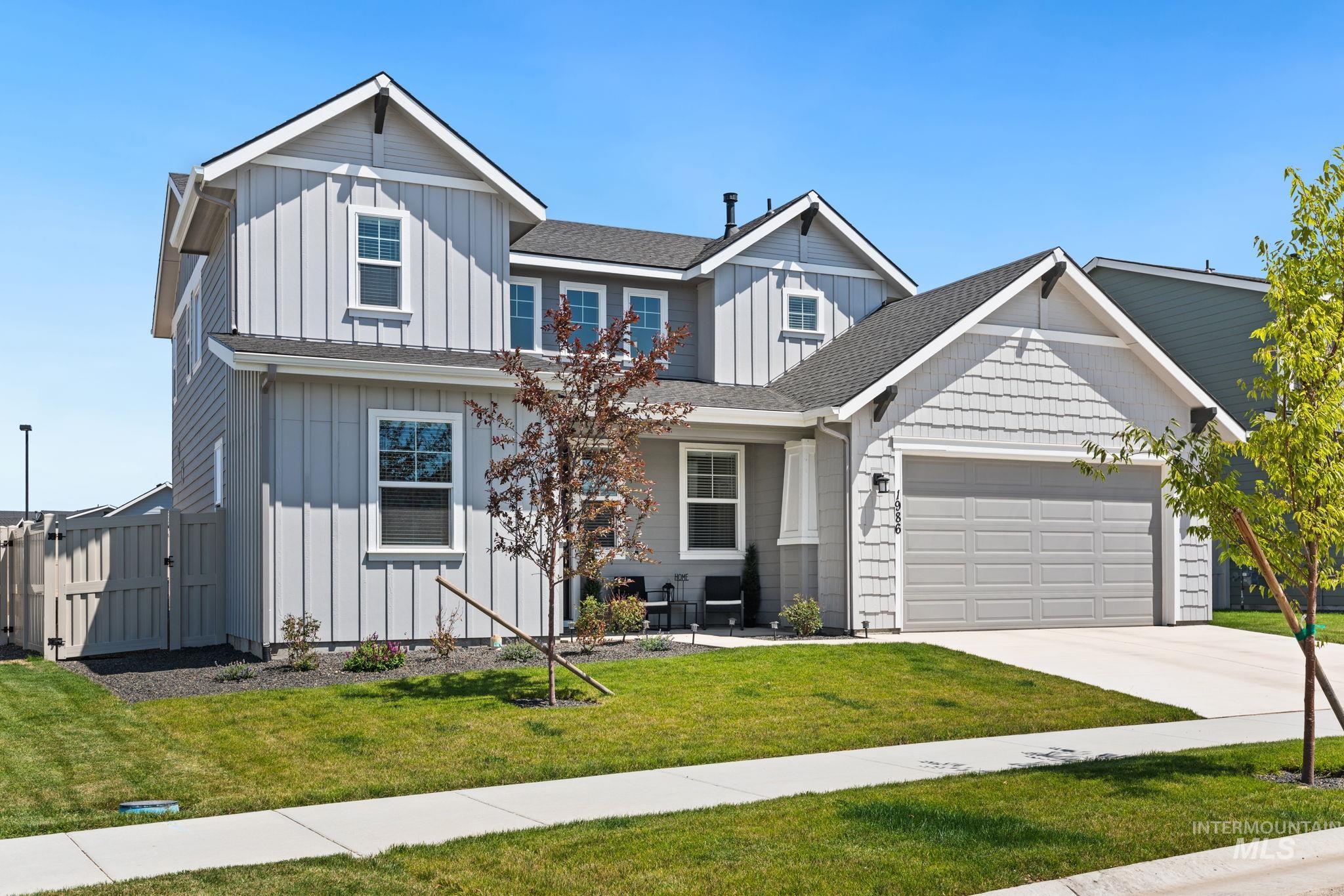 View of front facade with board and batten siding, driveway, an attached garage, and a gate