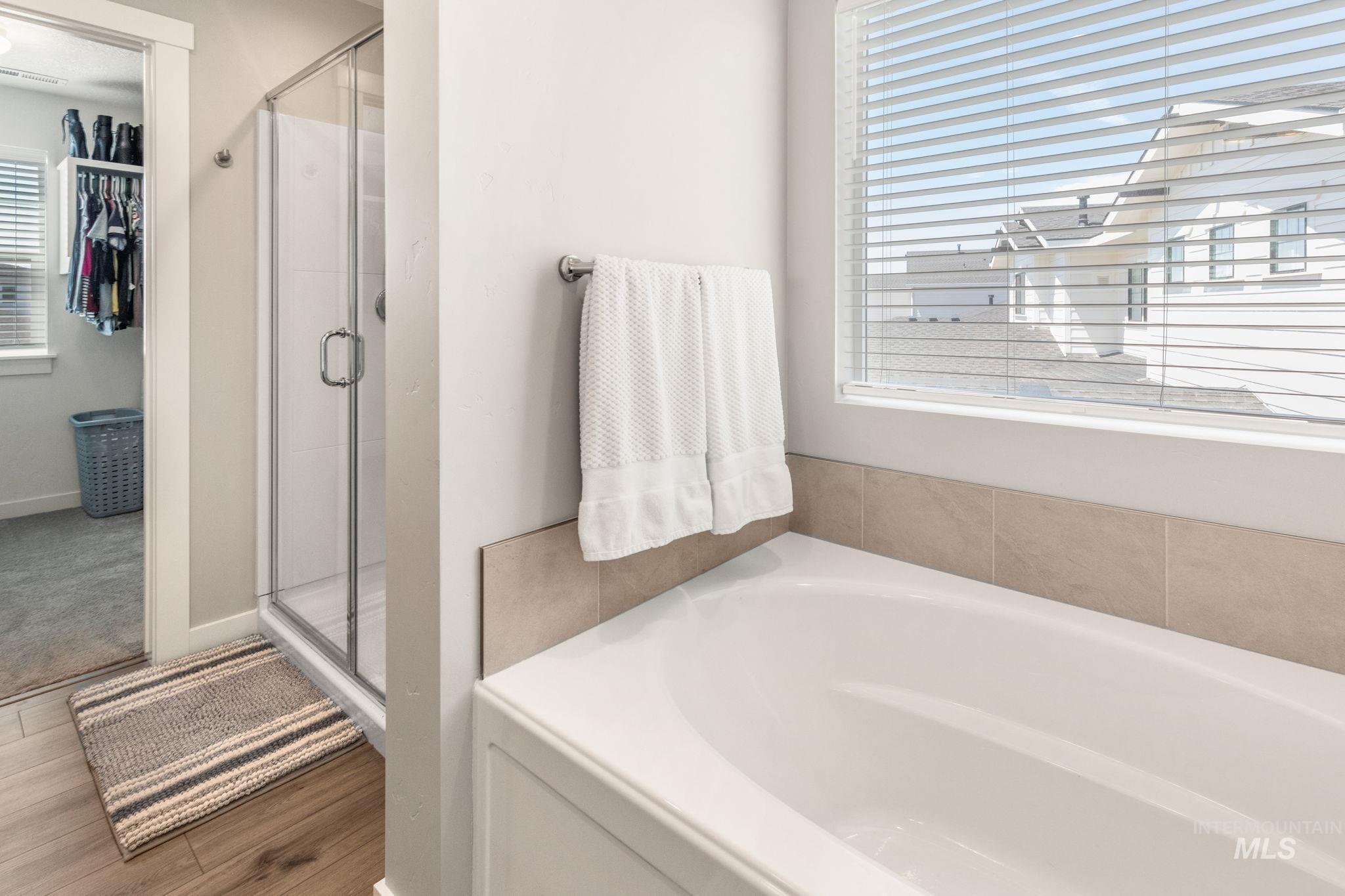 Full bath with a garden tub, a stall shower, wood finished floors, and a spacious closet