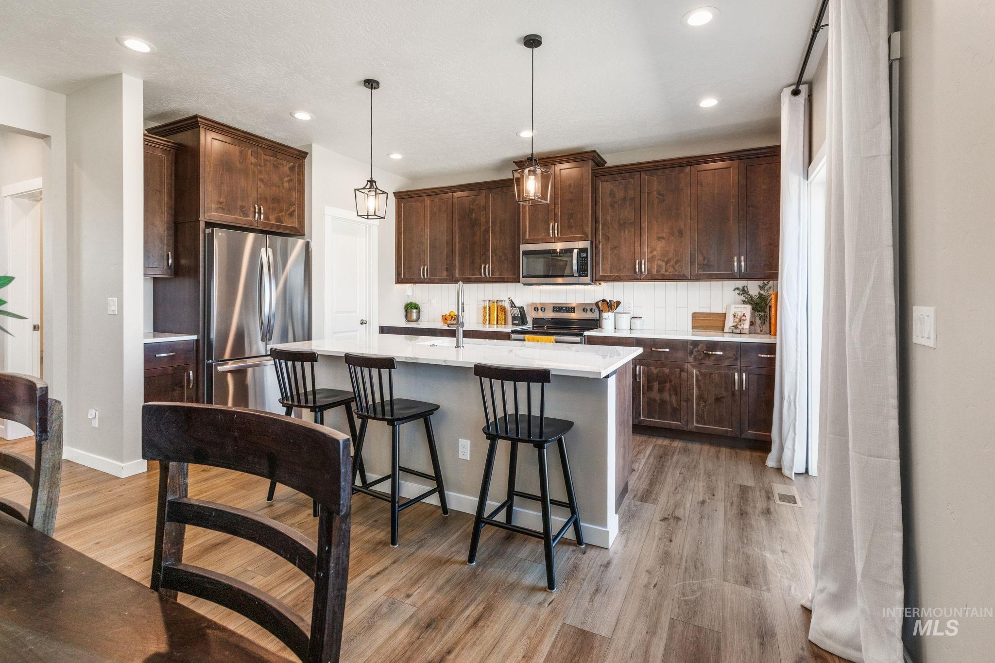 Kitchen with stainless steel appliances, light wood finished floors, light countertops, dark brown cabinets, and recessed lighting