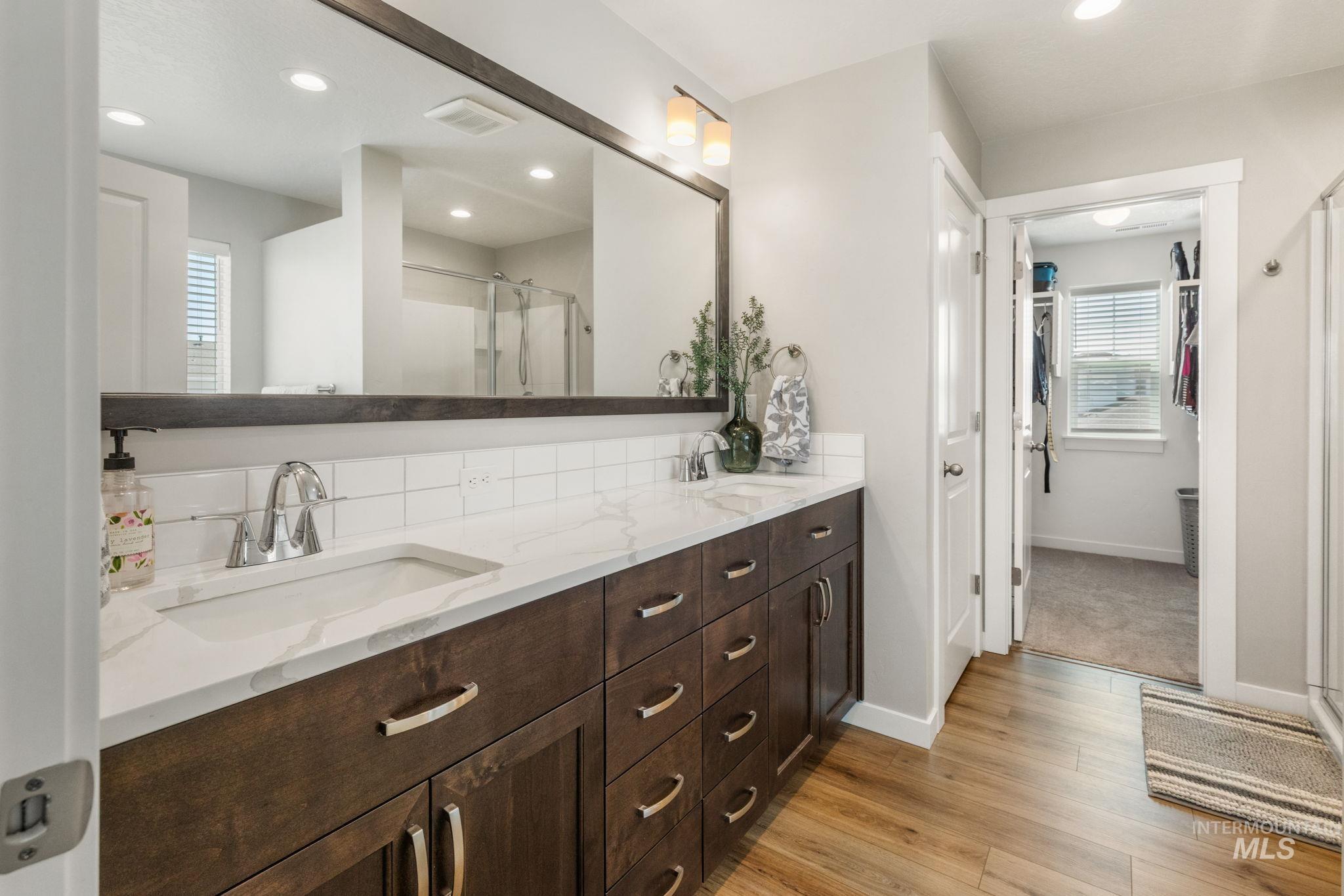 Full bath with wood finished floors, double vanity, a stall shower, and recessed lighting