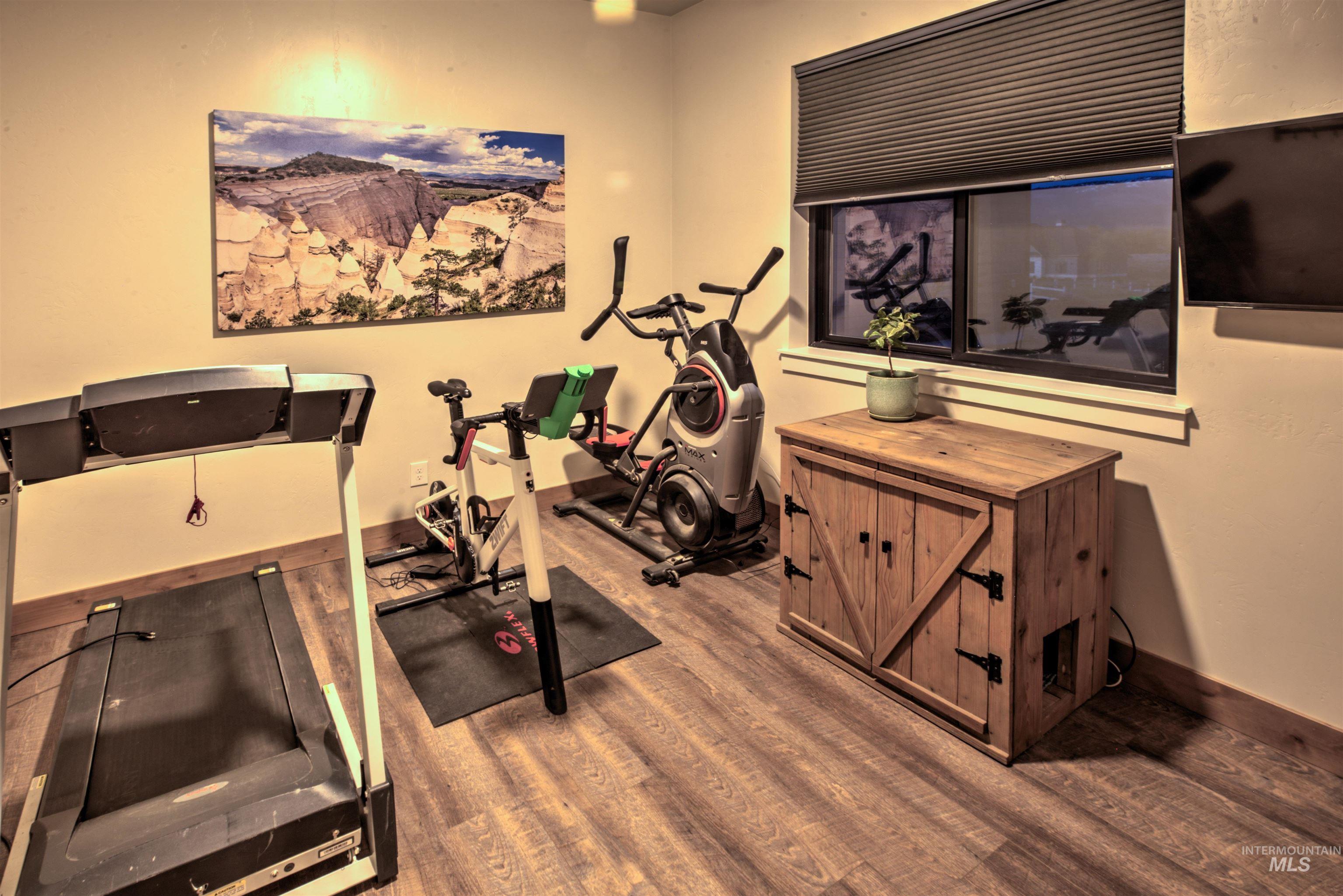 Room featuring wood-finish flooring, a window with a cellular shade, and a built-in wooden cabinet with barn-door style hardware