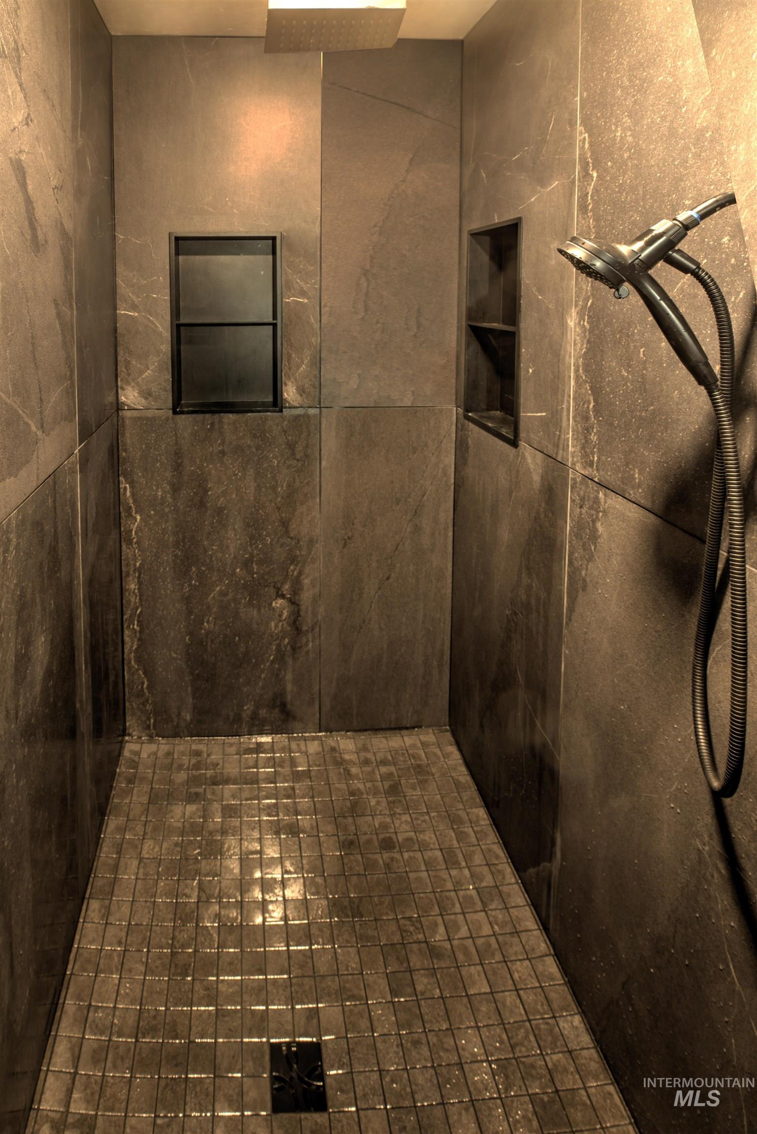 Walk-in shower featuring large format stone-finish wall tile, square mosaic floor tile, and a built-in shower niche