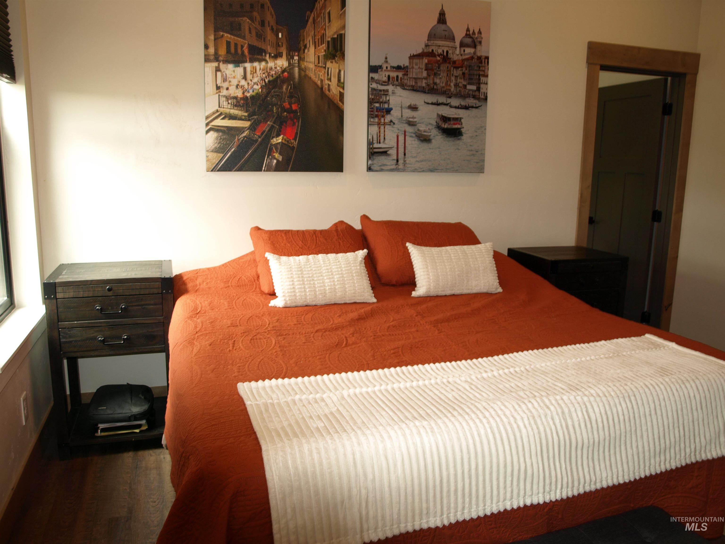 Bedroom featuring a window with blinds, wood-finish flooring, and a door with wood trim