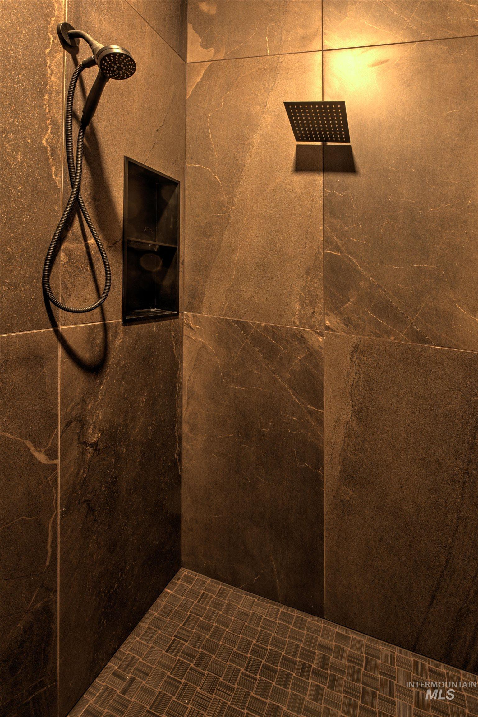 Shower stall featuring large format wall tiles, a built-in niche, a square rainfall showerhead, and a handheld shower attachment