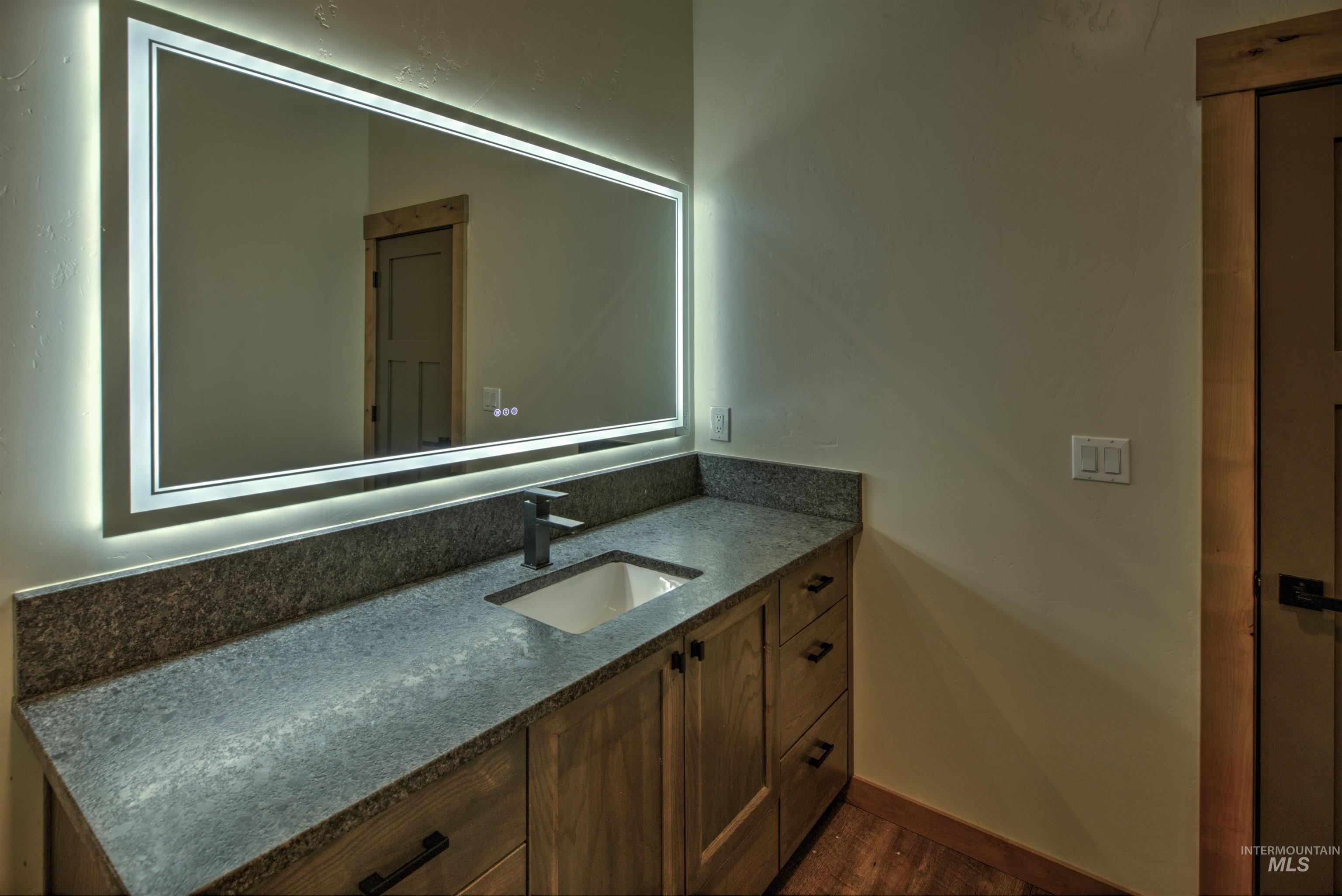 Backlit vanity mirror illuminating a rectangular undermount sink with a matte black faucet