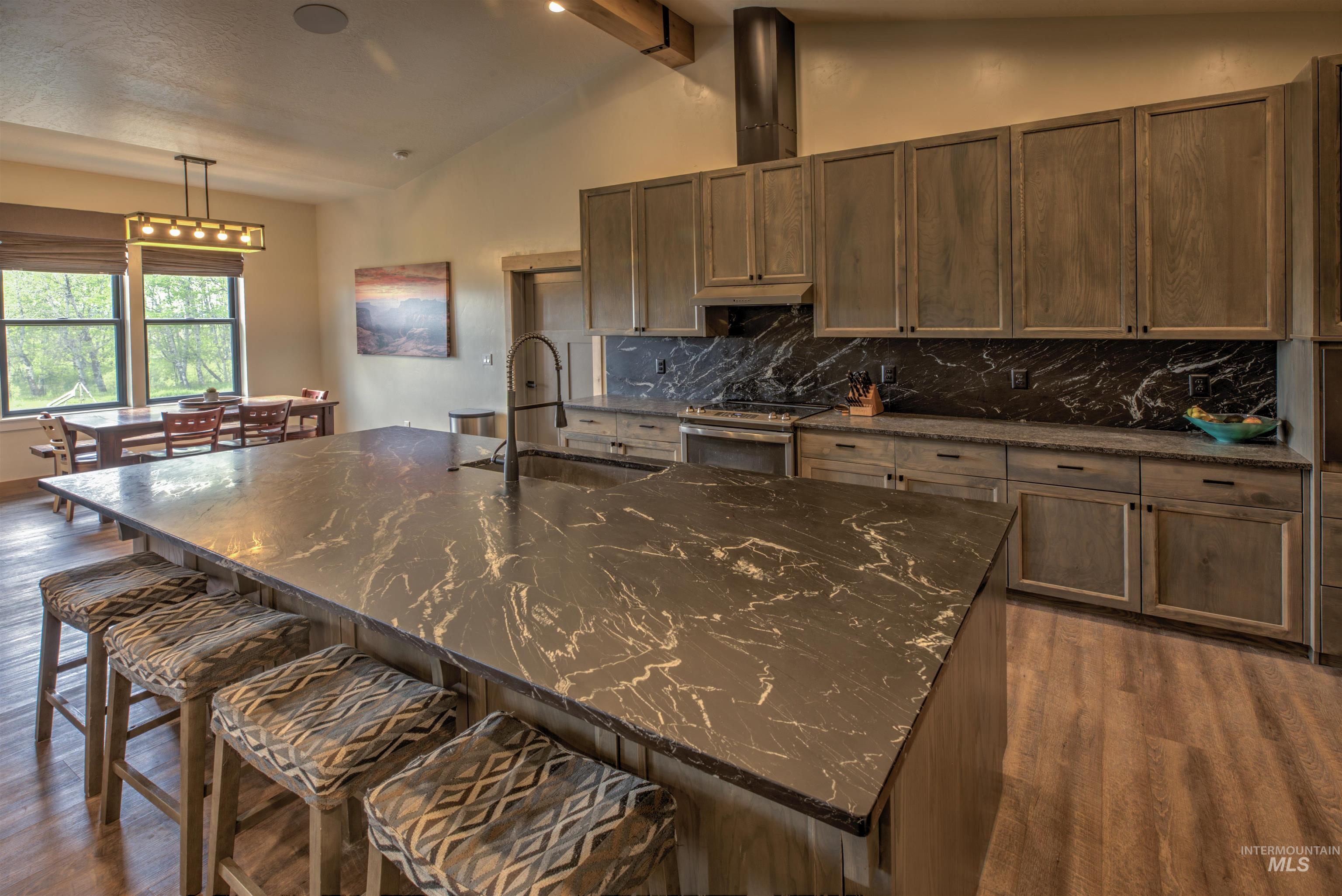 Spacious kitchen featuring a large central island with a built-in sink, dark marbled countertops, wood-finish cabinetry, and a matching backsplash