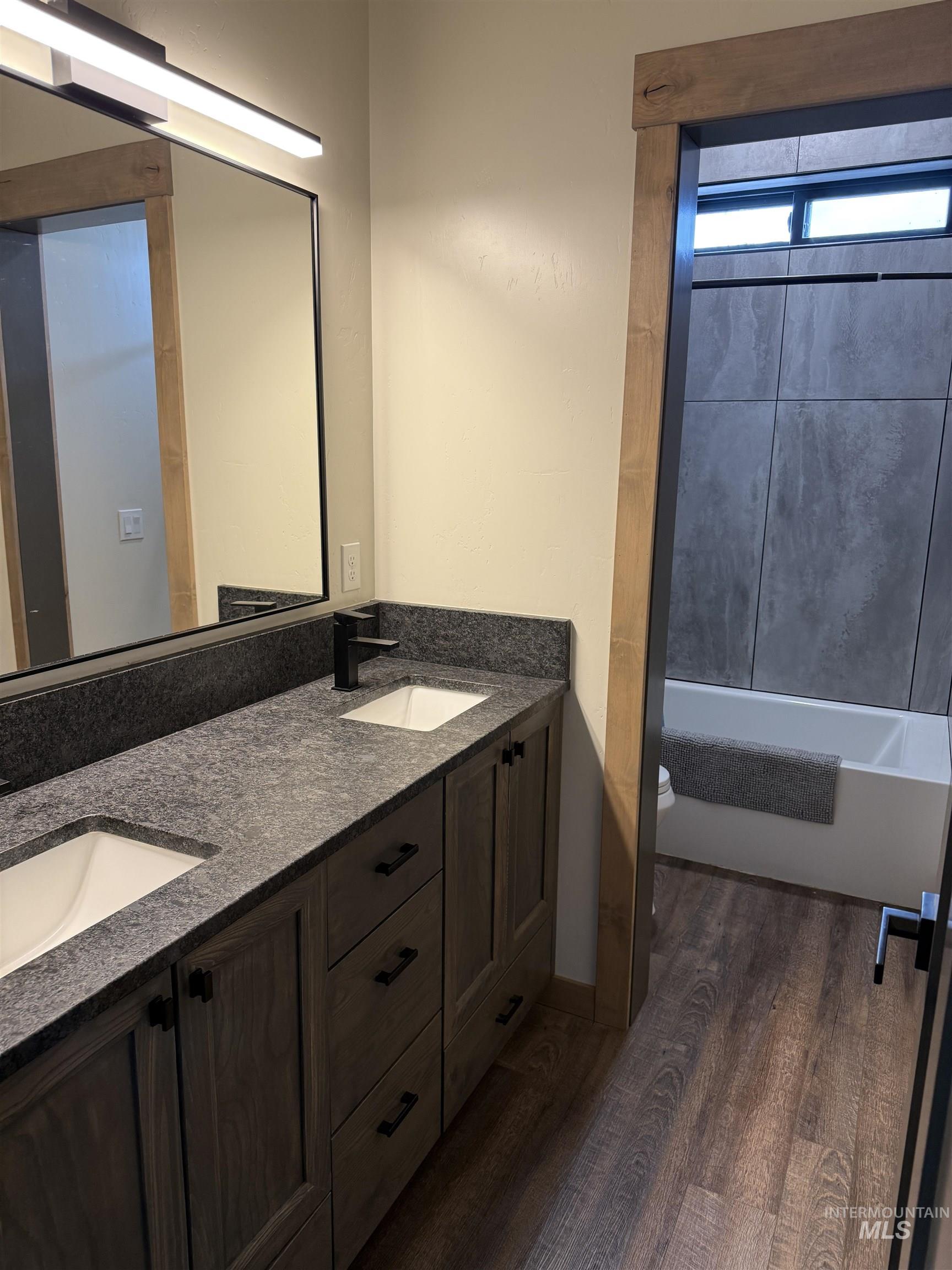Dual vanity featuring integrated sinks, dark stone countertops, and wood-finish cabinetry with matte black hardware