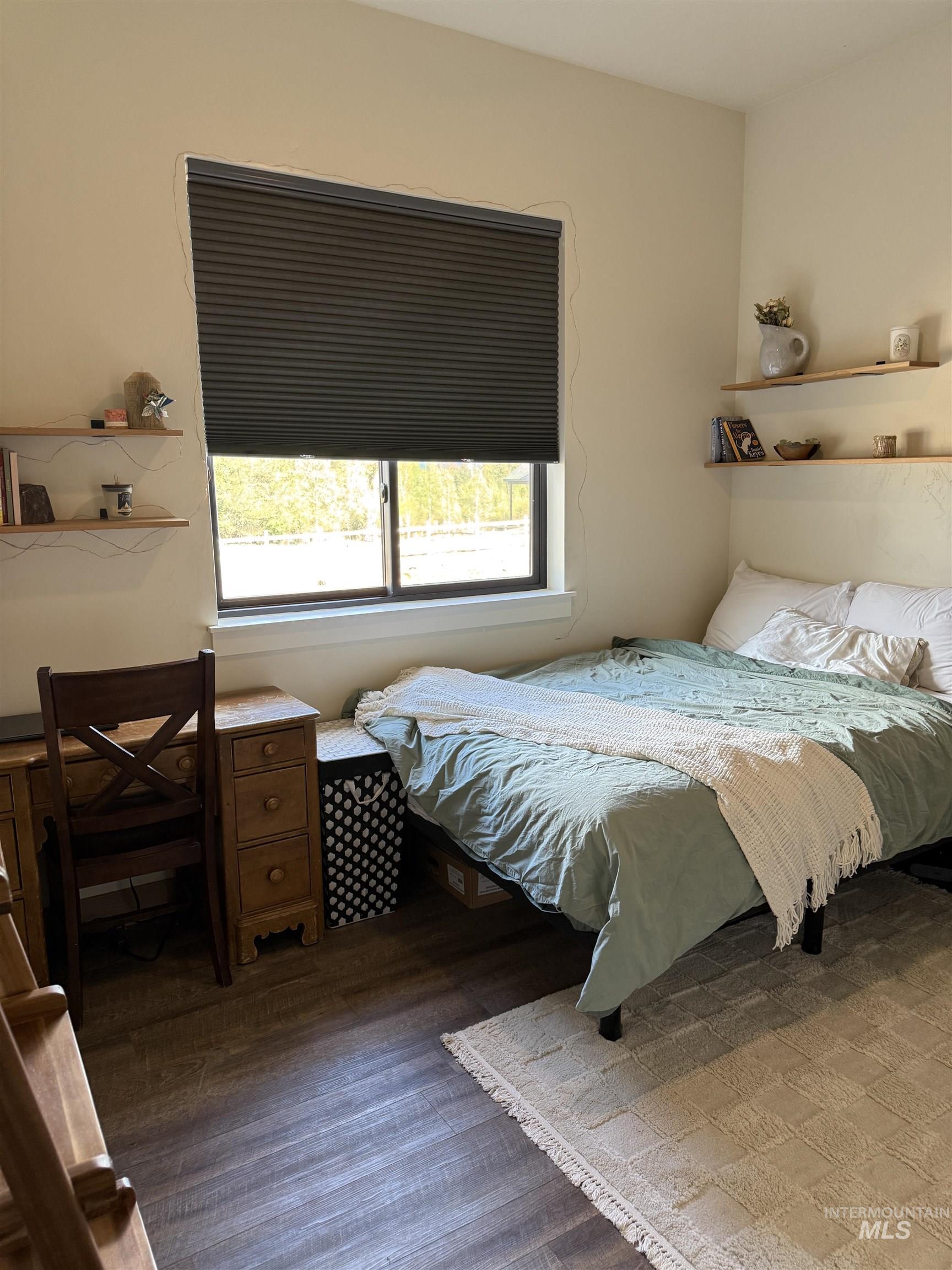 Windowed room featuring wood-finish flooring, light-toned walls, and multiple floating wall shelves