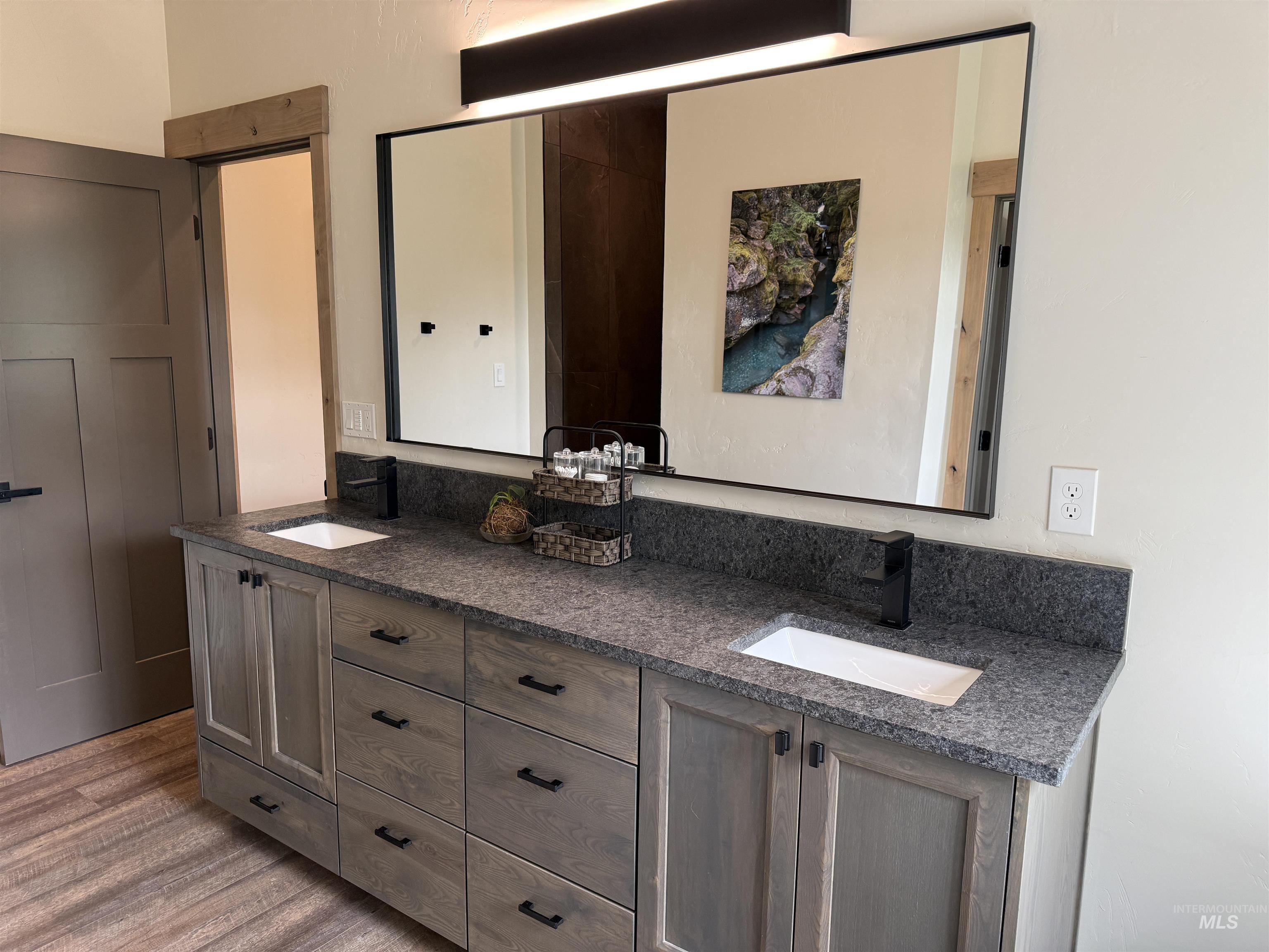 Double vanity featuring wood-finish cabinetry with black hardware, integrated rectangular sinks, and a stone-finish countertop with a matching backsplash