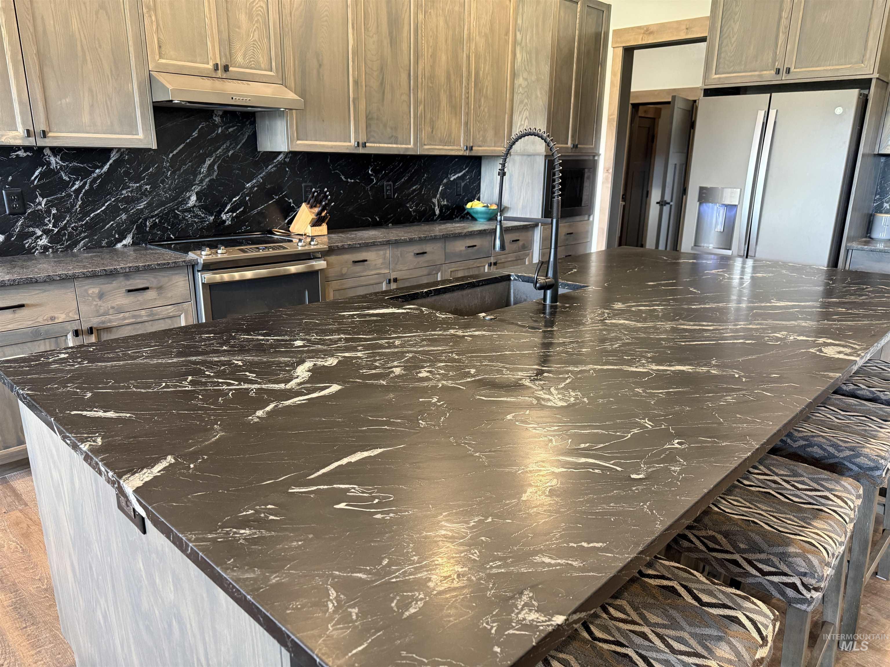 Expansive kitchen island featuring a dark countertop with white veining, an undermount sink, and a black gooseneck faucet