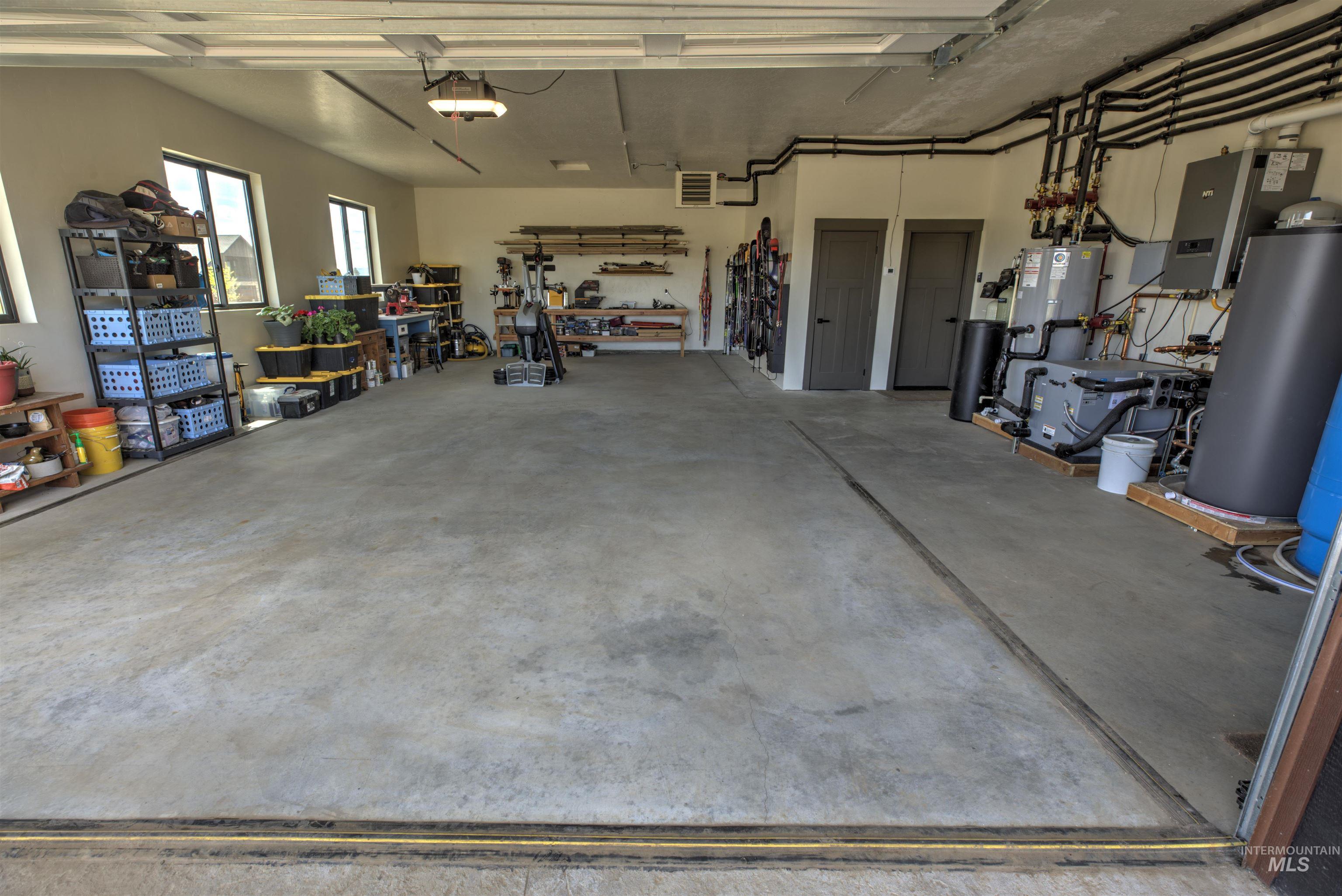 Spacious garage featuring a concrete floor, multiple windows, two interior doors, comprehensive utility systems, and overhead lighting