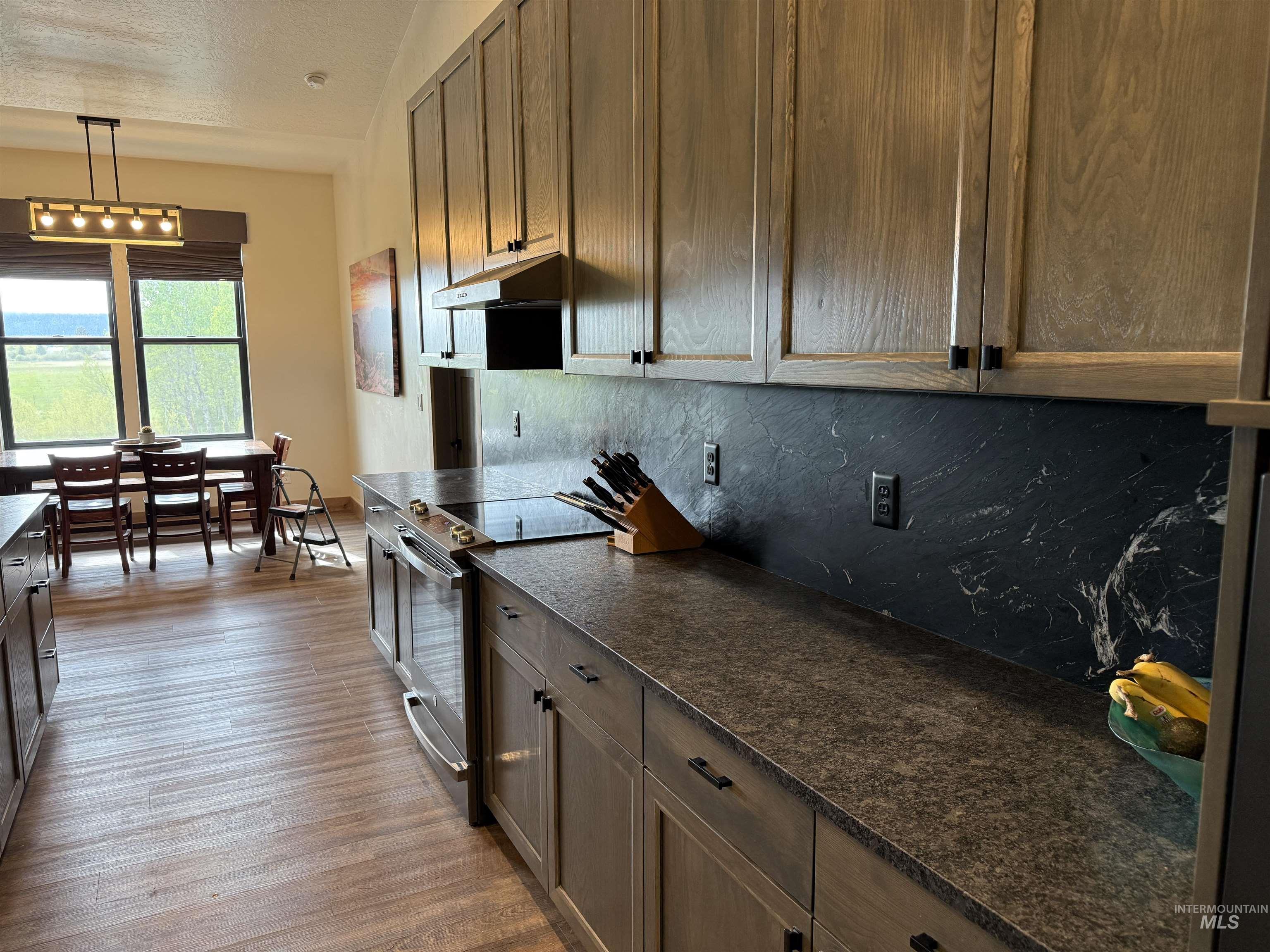 Kitchen showcasing wood-finish cabinetry, dark countertops, and a striking dark marble-patterned backsplash