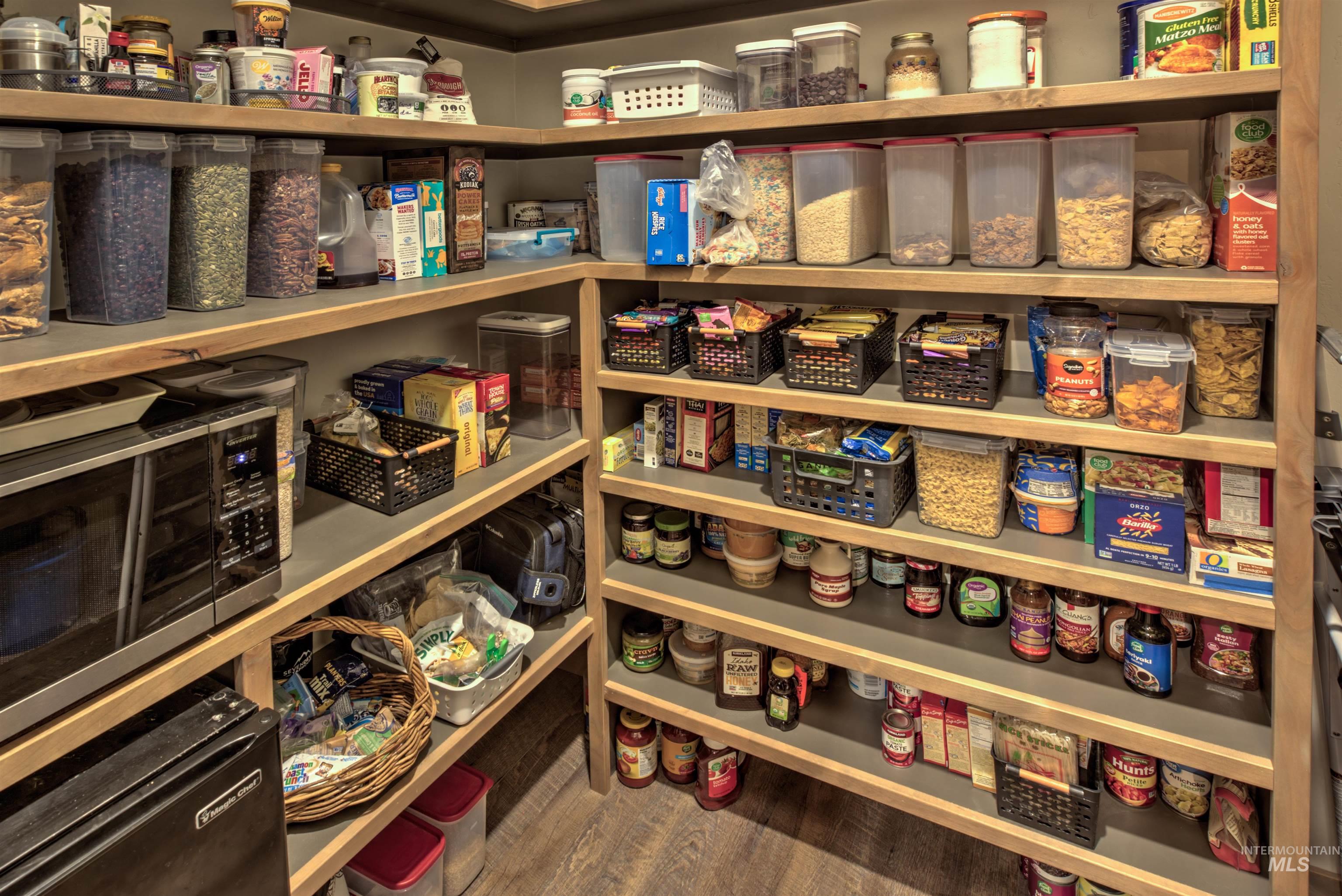 Spacious pantry featuring extensive wood-finish shelving, built-in microwave, and wood-finish flooring