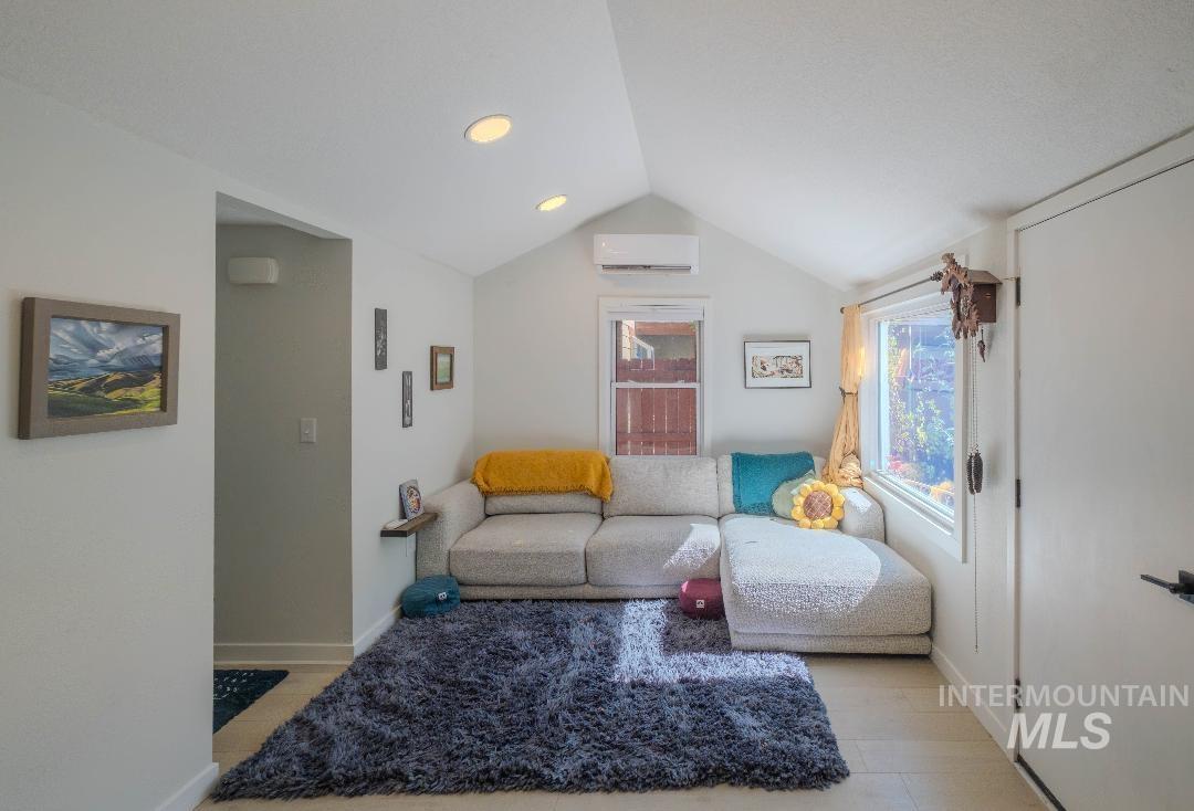 Living area featuring vaulted ceiling, light wood-style flooring, an AC wall unit, and recessed lighting