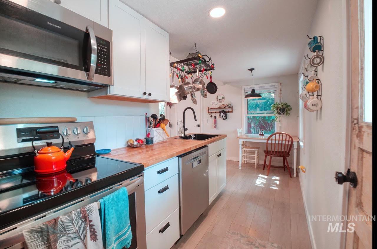 Kitchen featuring stainless steel appliances, white cabinets, pendant lighting, light wood-style floors, and wooden counters