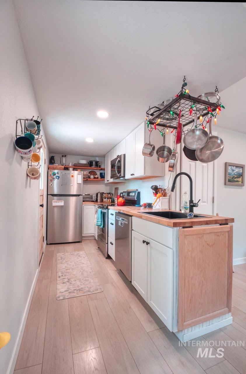 Kitchen featuring appliances with stainless steel finishes, white cabinets, open shelves, light wood-style flooring, and recessed lighting