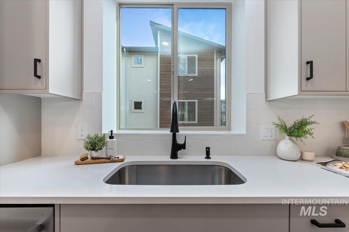Kitchen with decorative backsplash, white cabinetry, and light stone countertops