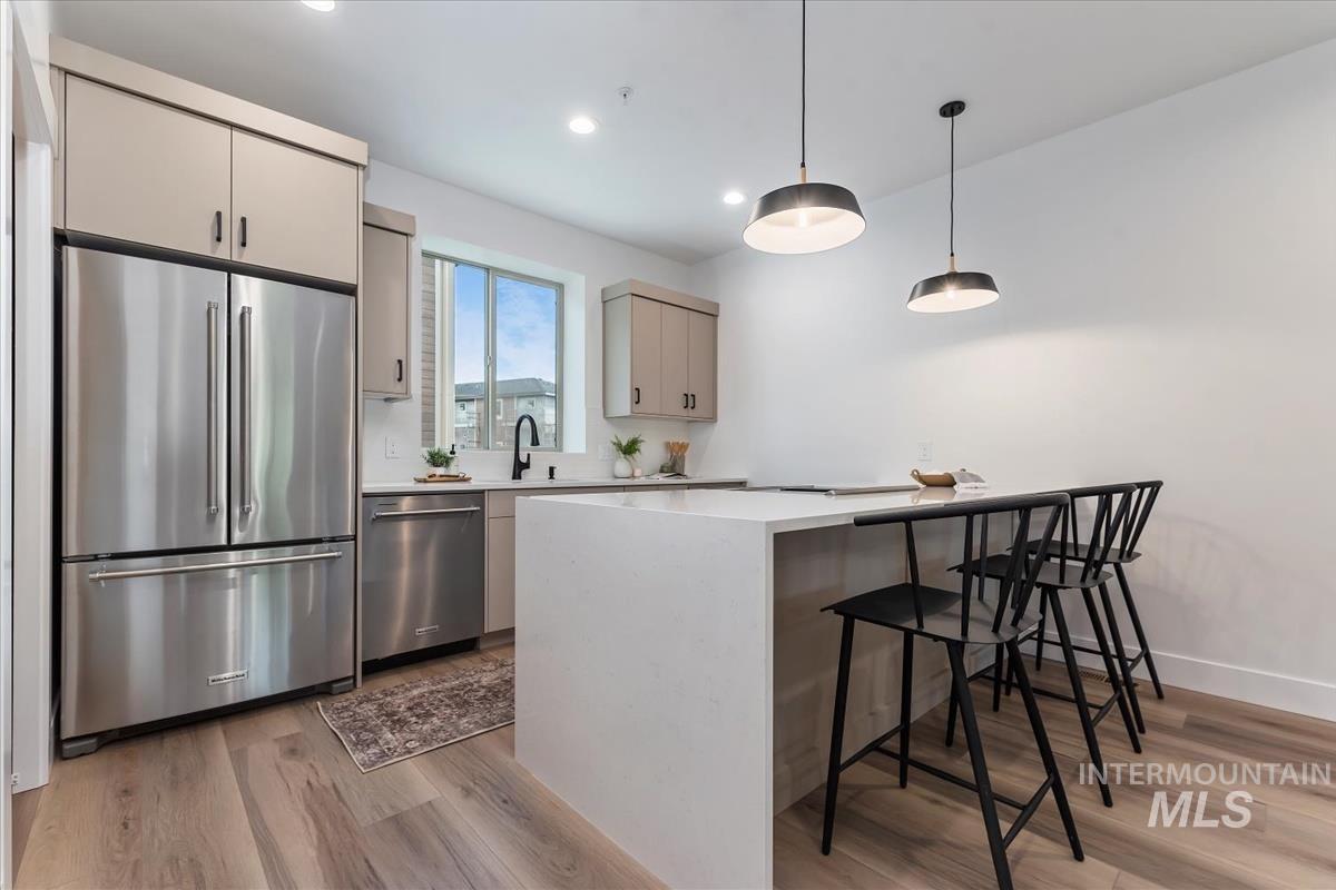 Kitchen with stainless steel appliances, pendant lighting, a kitchen breakfast bar, light stone counters, and light wood finished floors