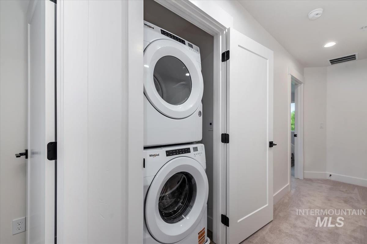 Laundry room featuring light colored carpet, estacked washer and dryer, and recessed lighting