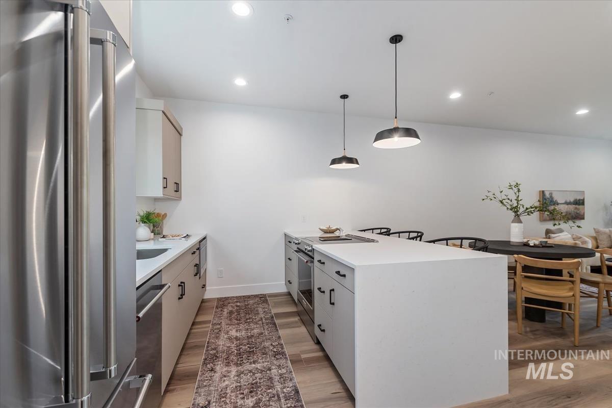 Kitchen with appliances with stainless steel finishes, a peninsula, hanging light fixtures, light stone countertops, and light wood-type flooring