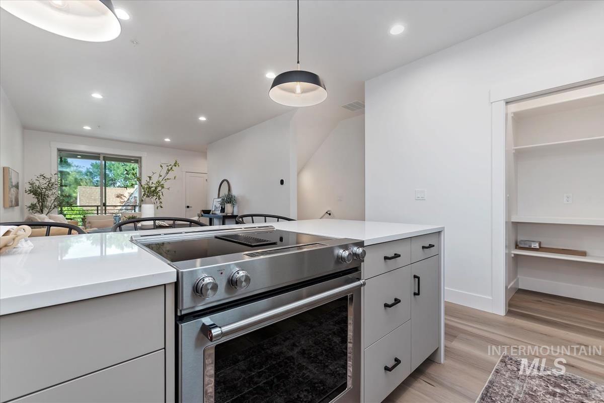 Kitchen featuring stainless steel electric range, light wood-style floors, hanging light fixtures, recessed lighting, and light stone counters