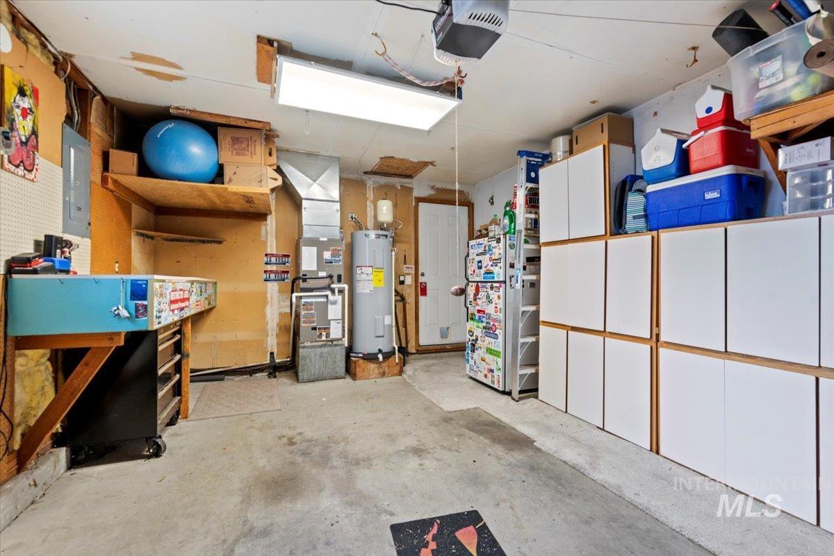 Garage featuring a garage door opener, water heater, heating unit, electric panel, and freestanding refrigerator