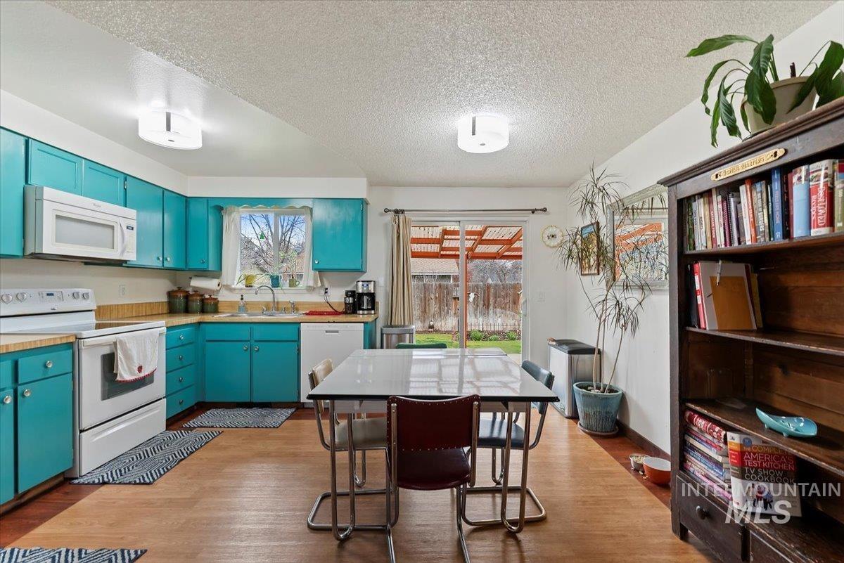 Kitchen featuring white appliances, light countertops, blue cabinets, a textured ceiling, and light wood-style floors