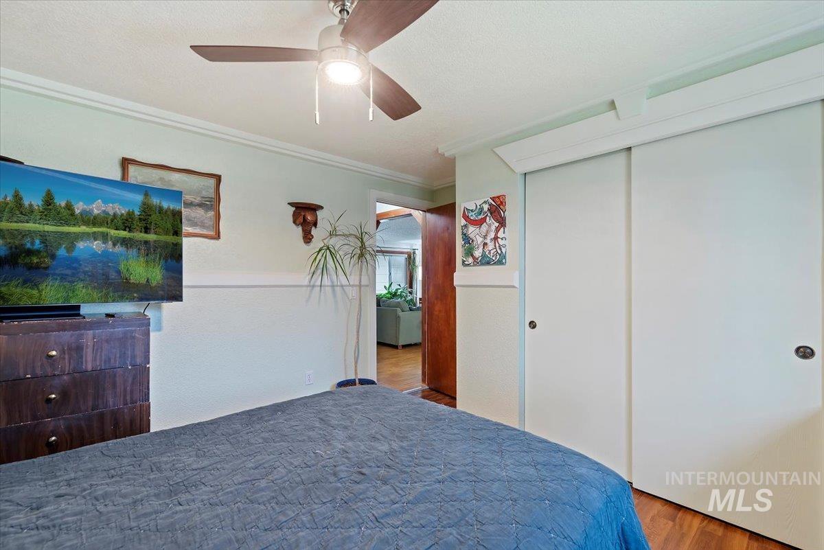 Bedroom featuring wood finished floors, ornamental molding, a ceiling fan, a closet, and a textured ceiling