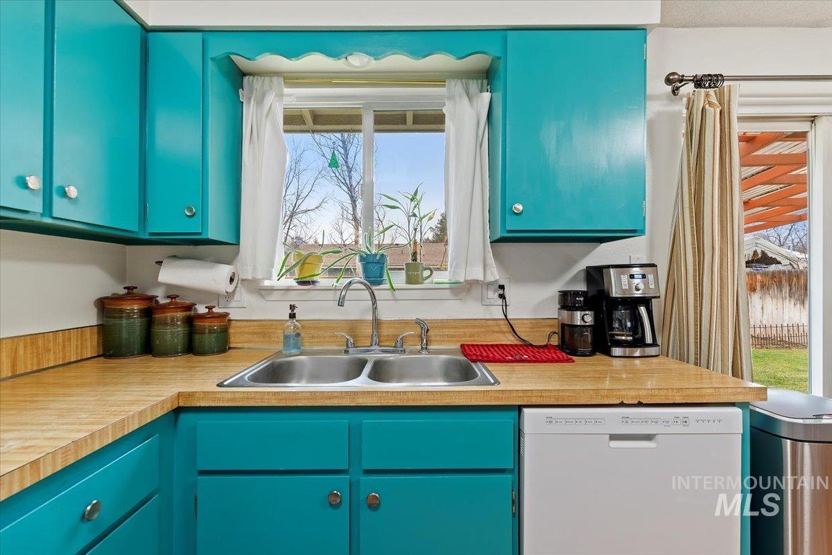 Kitchen featuring white dishwasher, blue cabinets, light countertops, and plenty of natural light