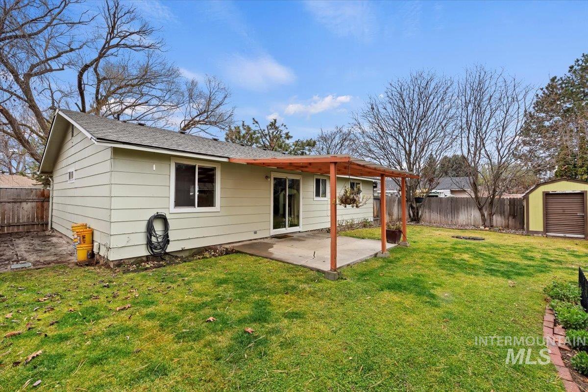 Rear view of house featuring a patio, a fenced backyard, a storage shed, and roof with shingles