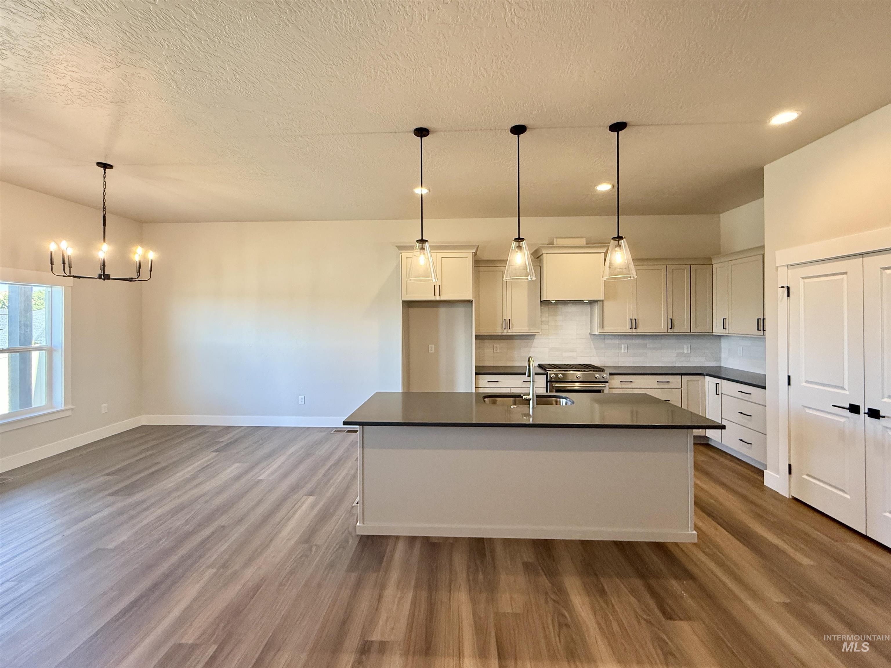 Kitchen featuring pendant lighting, a textured ceiling, dark wood-style floors, tasteful backsplash, and a chandelier