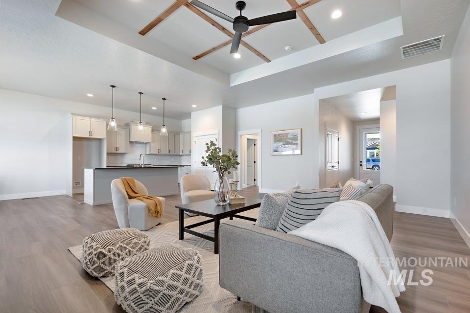 Living room featuring a raised ceiling, ceiling fan, light wood finished floors, and recessed lighting