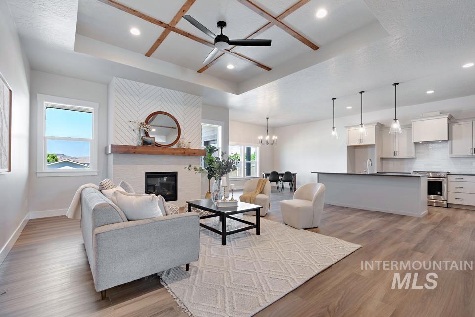 Living area featuring a tray ceiling, light wood-style floors, a large fireplace, a chandelier, and ceiling fan
