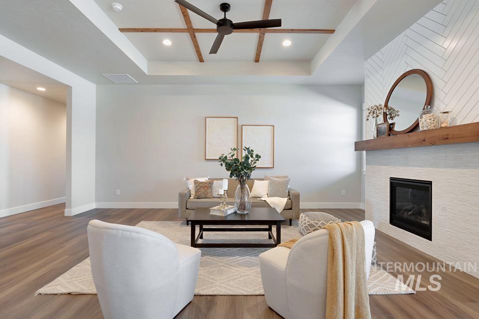 Living area with a tile fireplace, wood finished floors, a tray ceiling, recessed lighting, and a ceiling fan