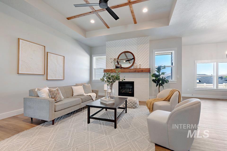 Living area featuring a raised ceiling, light wood-type flooring, a large fireplace, a ceiling fan, and recessed lighting