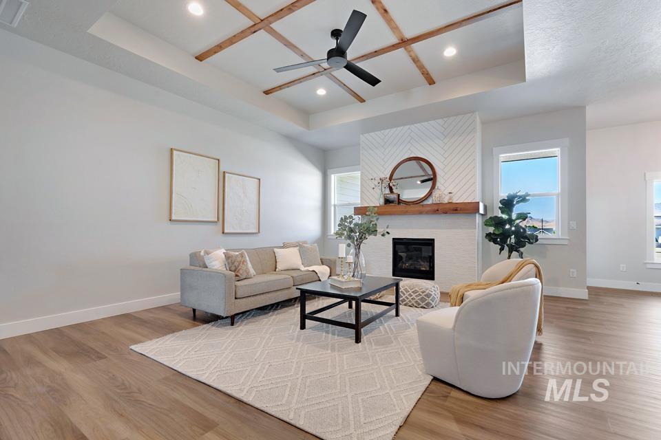 Living room featuring a tray ceiling, a fireplace, wood finished floors, a ceiling fan, and recessed lighting