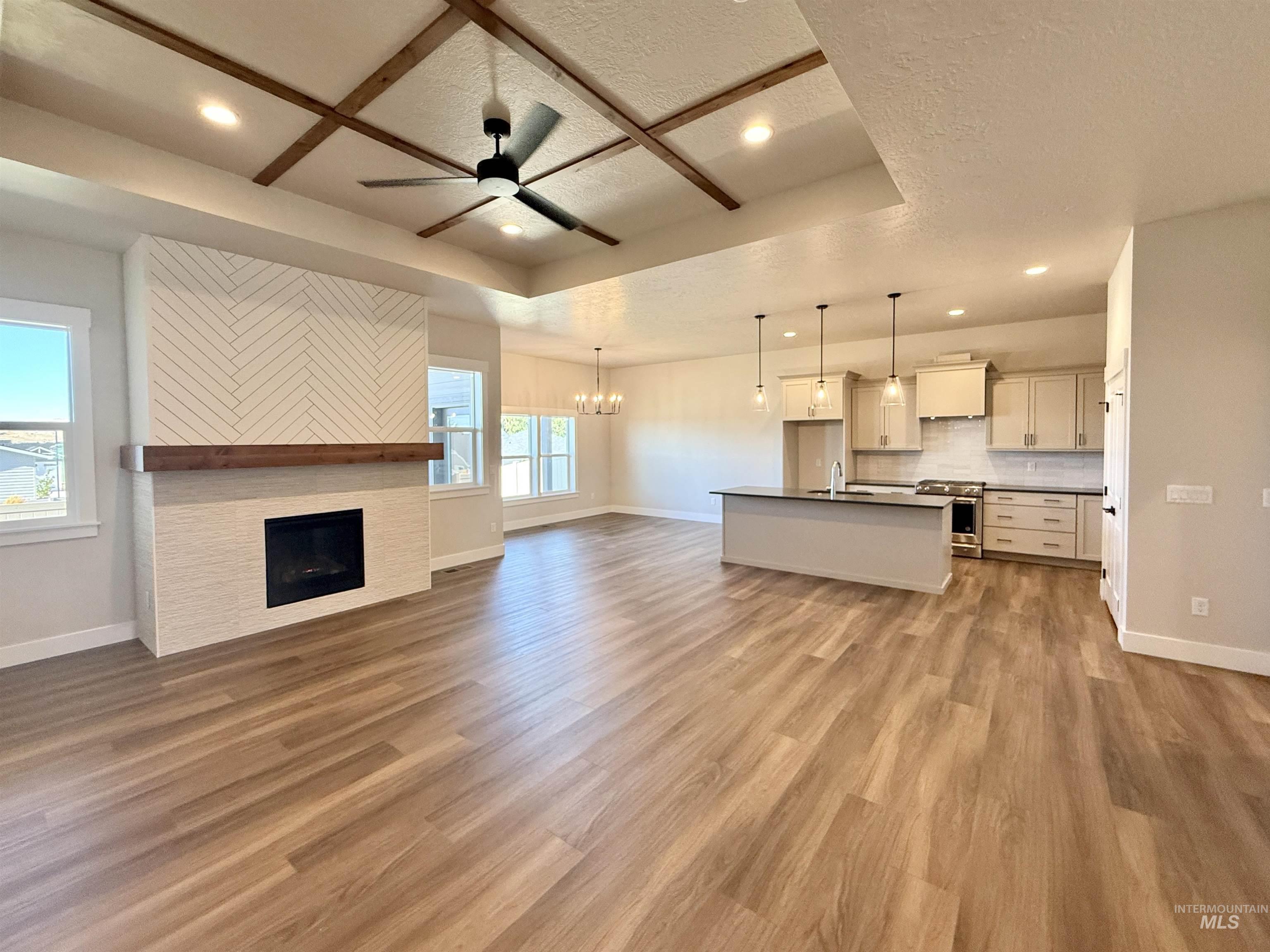 Unfurnished living room with a chandelier, a ceiling fan, recessed lighting, a raised ceiling, and light wood finished floors