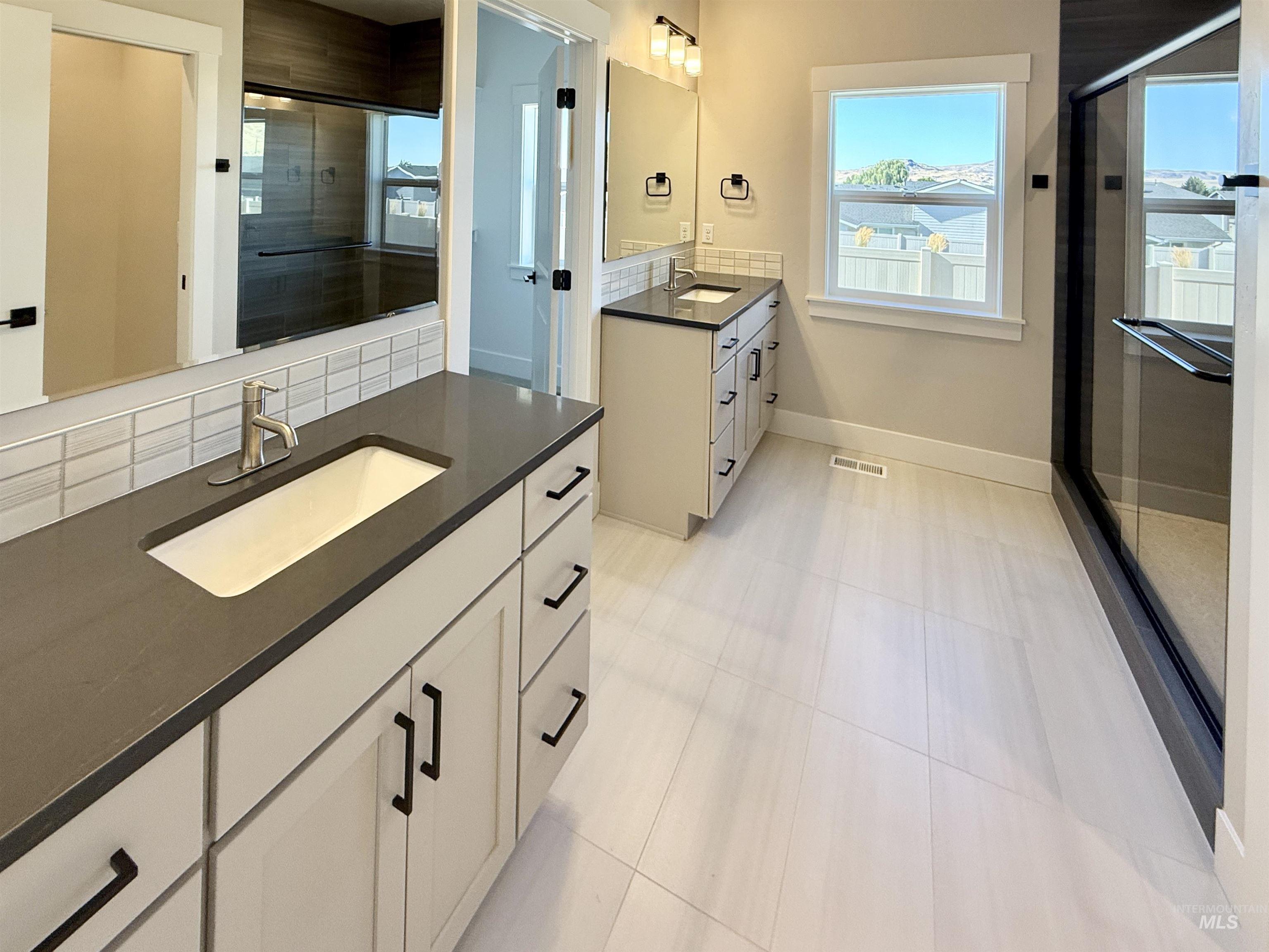 Bathroom featuring plenty of natural light, a stall shower, vanity, and backsplash